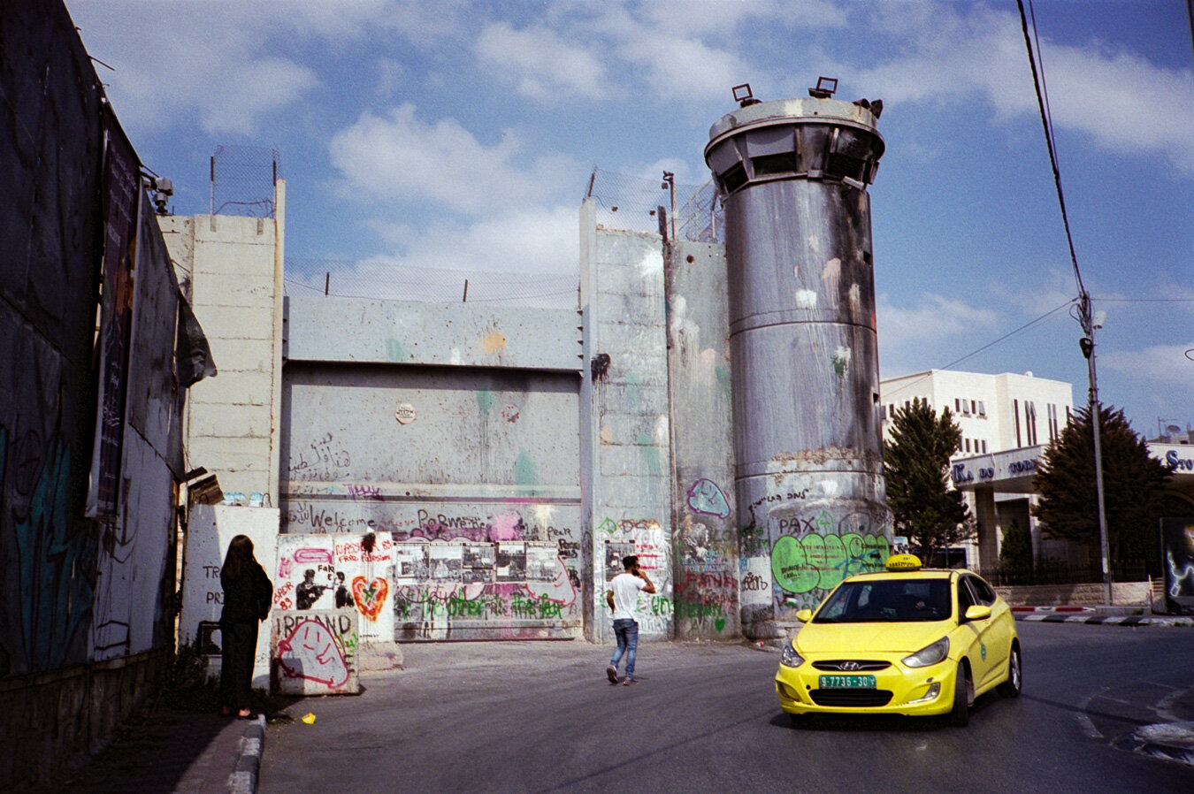 A yellow car beside a concrete wall and tower