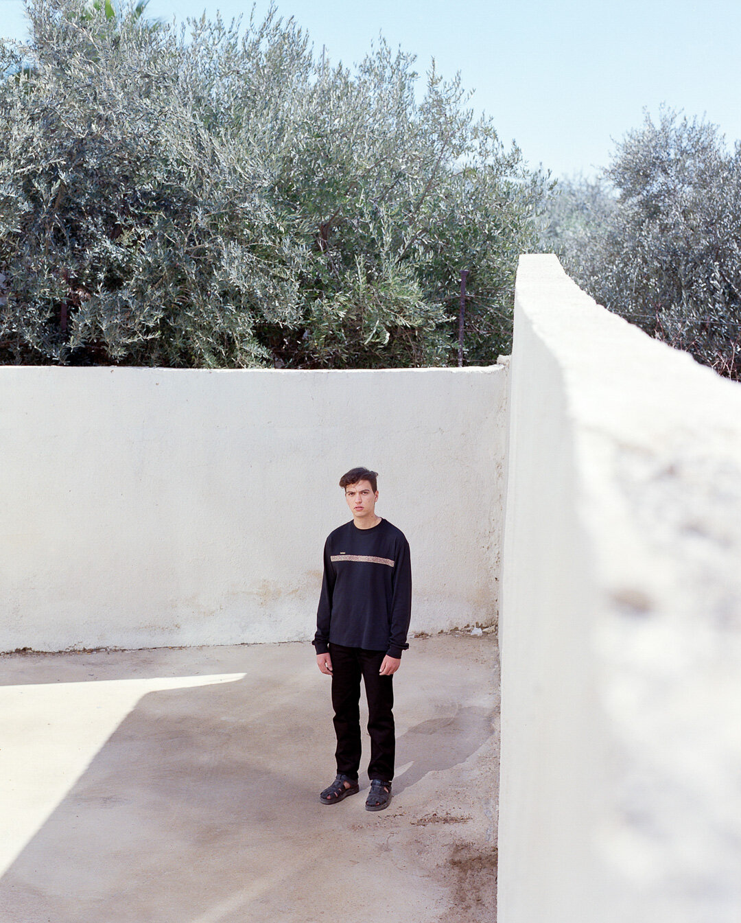 A person standing inside a walled courtyard, with trees above.