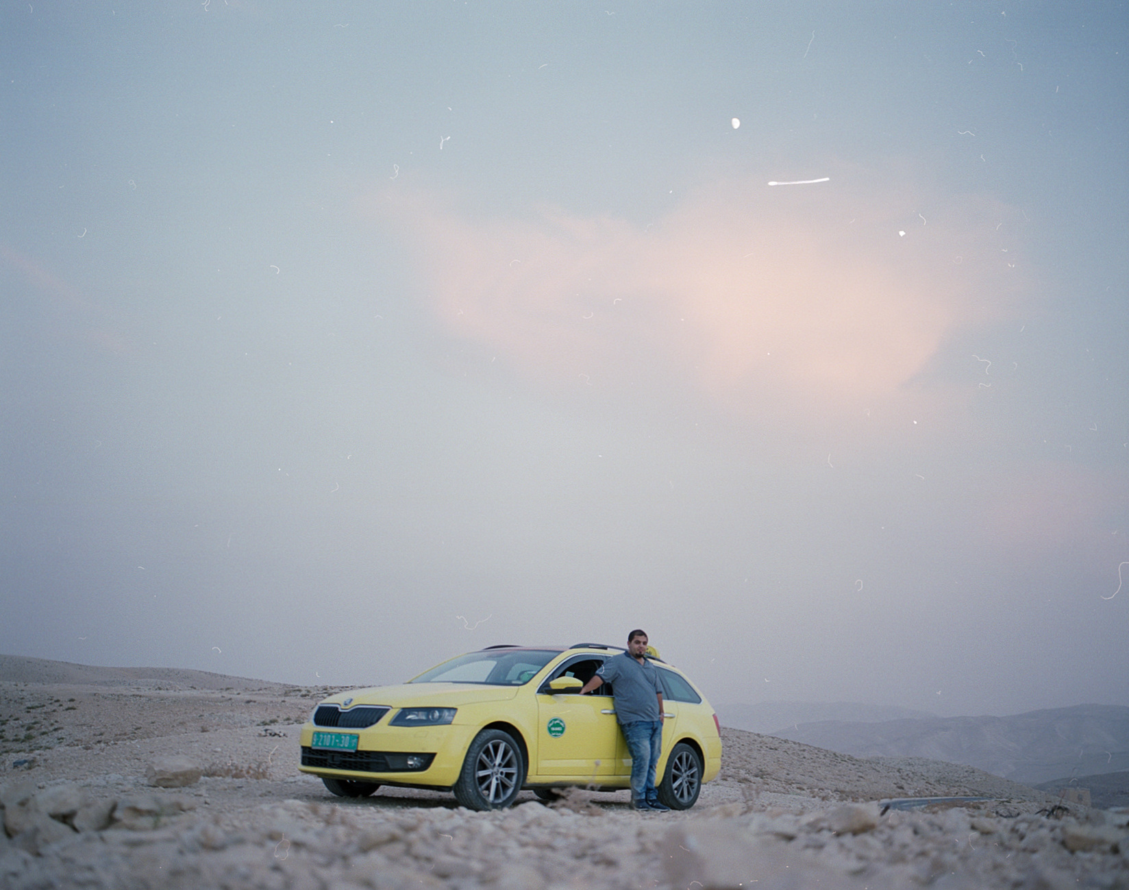 A yellow taxi on a hill at dusk.