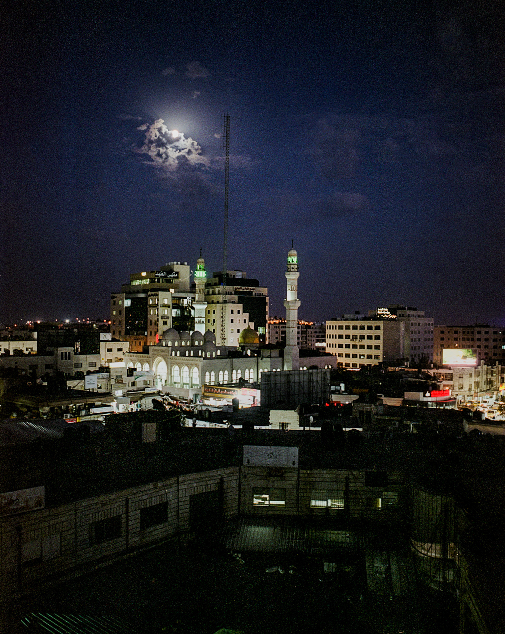 The moon above illuminated buildings at night.