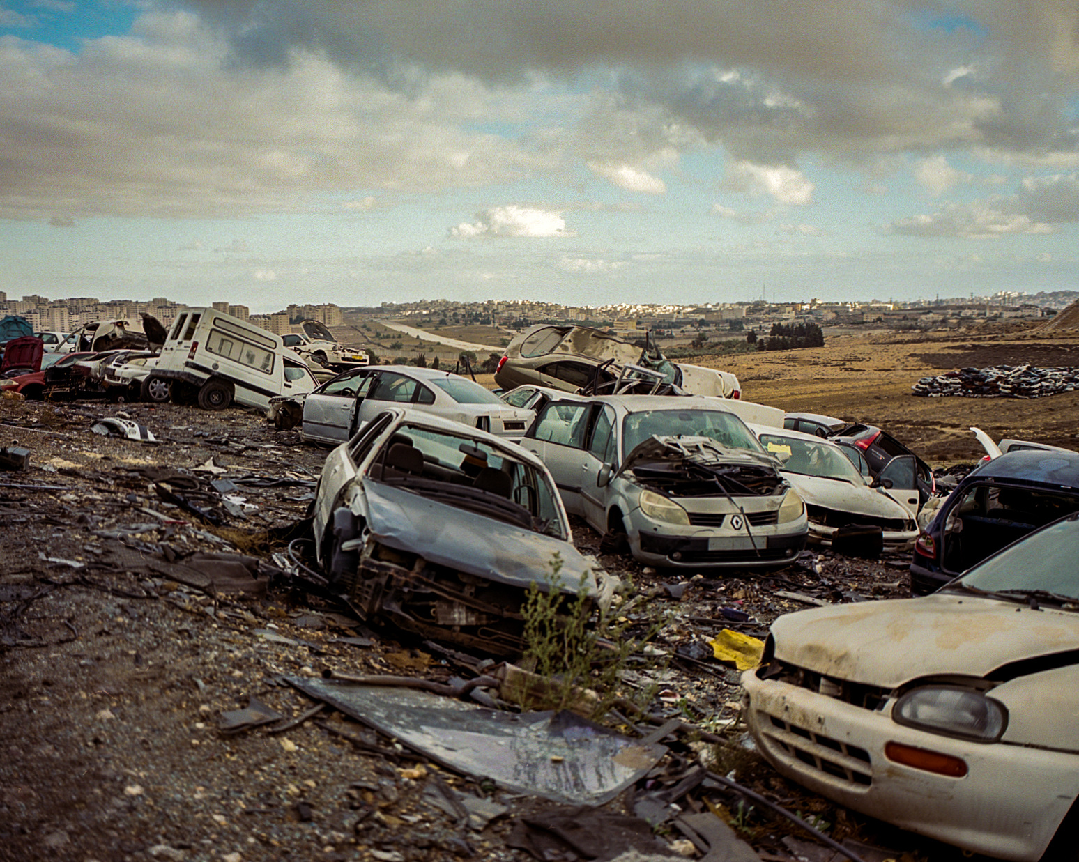 Wrecked cars in a scrapyard beneath a cloudy sky.