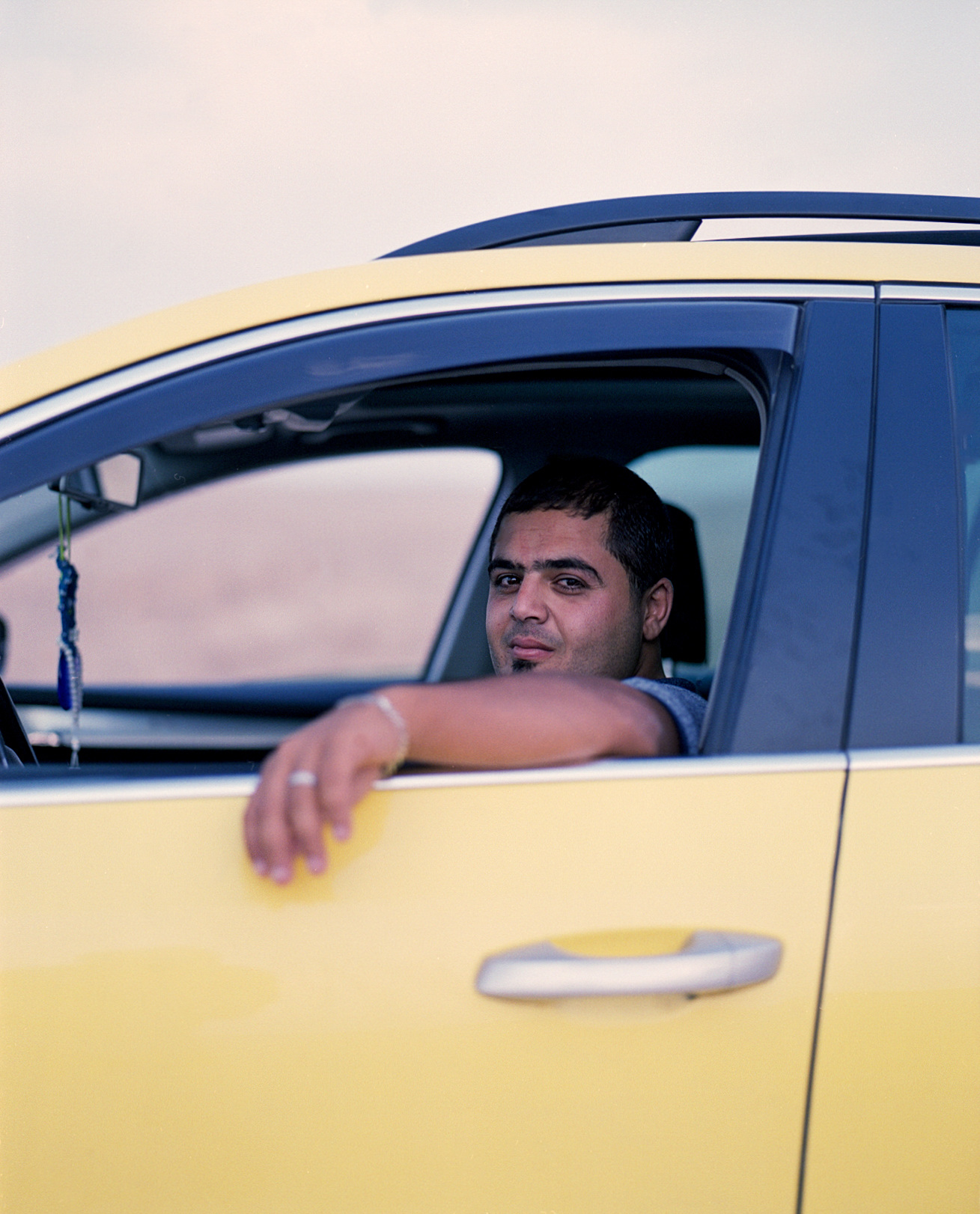 A driver resting an arm on the open window of a yellow taxi.