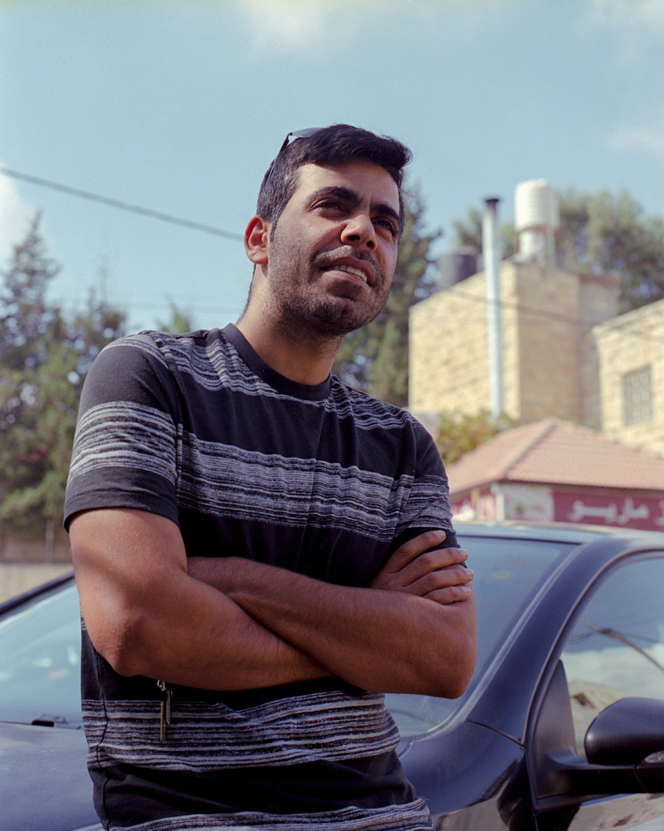 A man standing with folded arms beside a car.