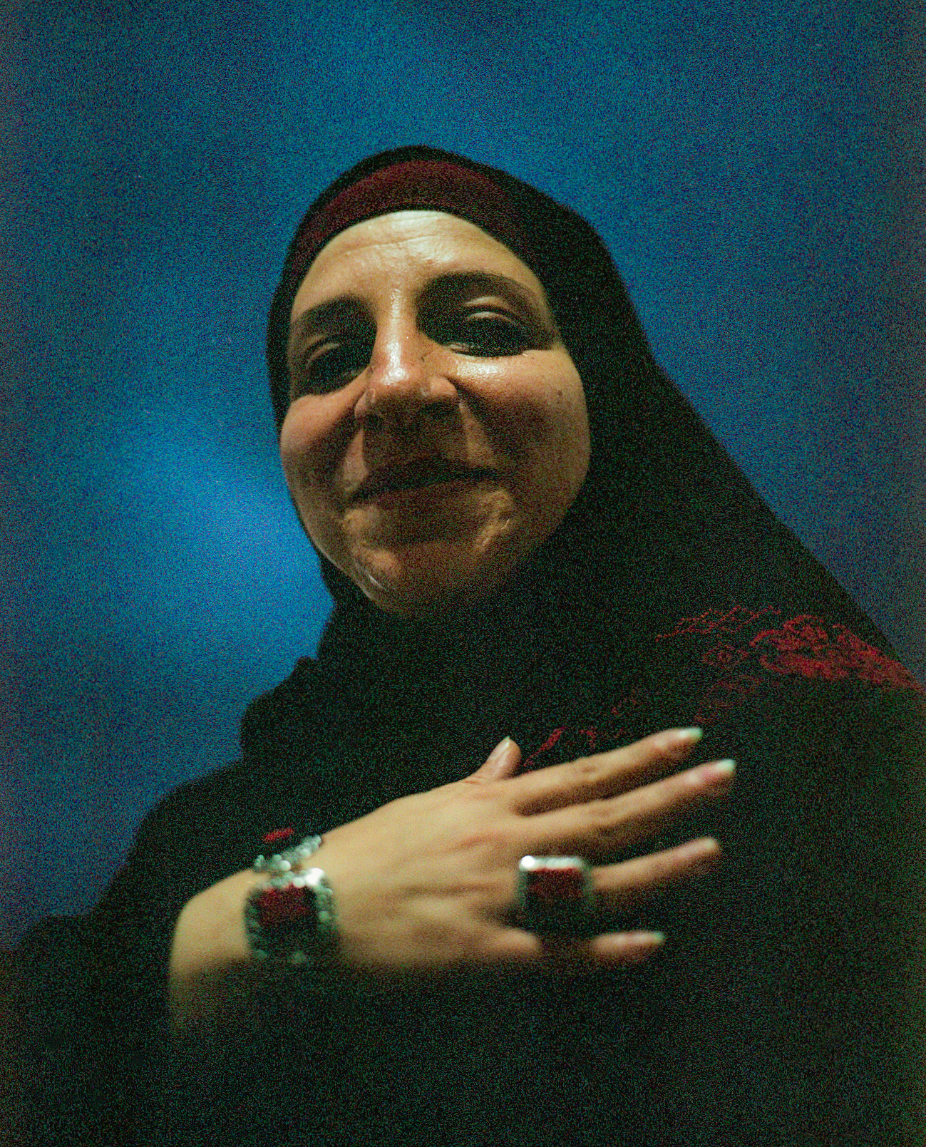 A woman seated against a blue wall.