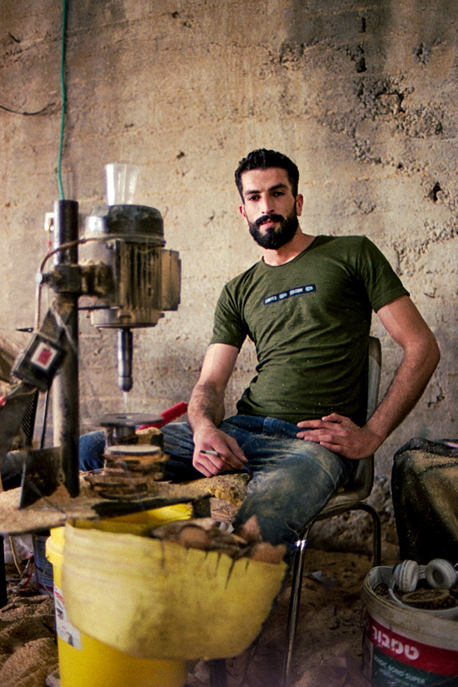 A seated man beside workshop machinery.