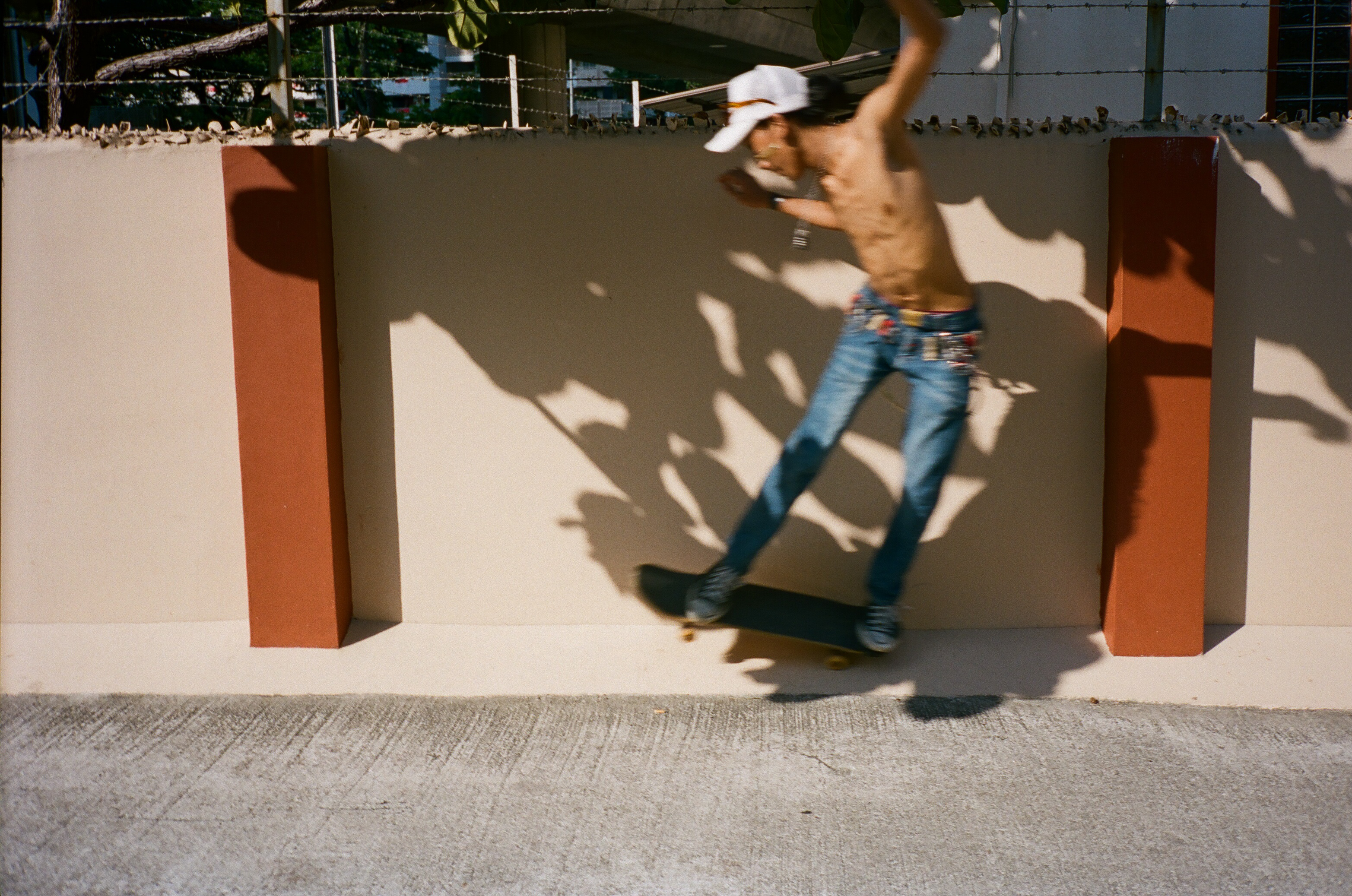 A skateboarder in motion beside a sunlit wall.