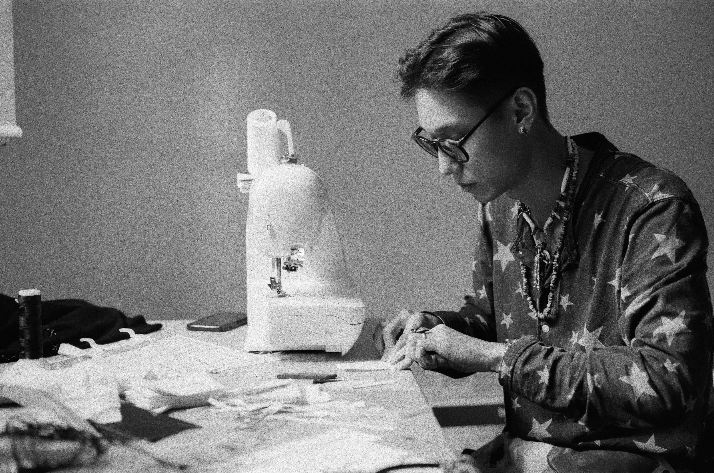 A person working with material at a table beside a sewing machine.
