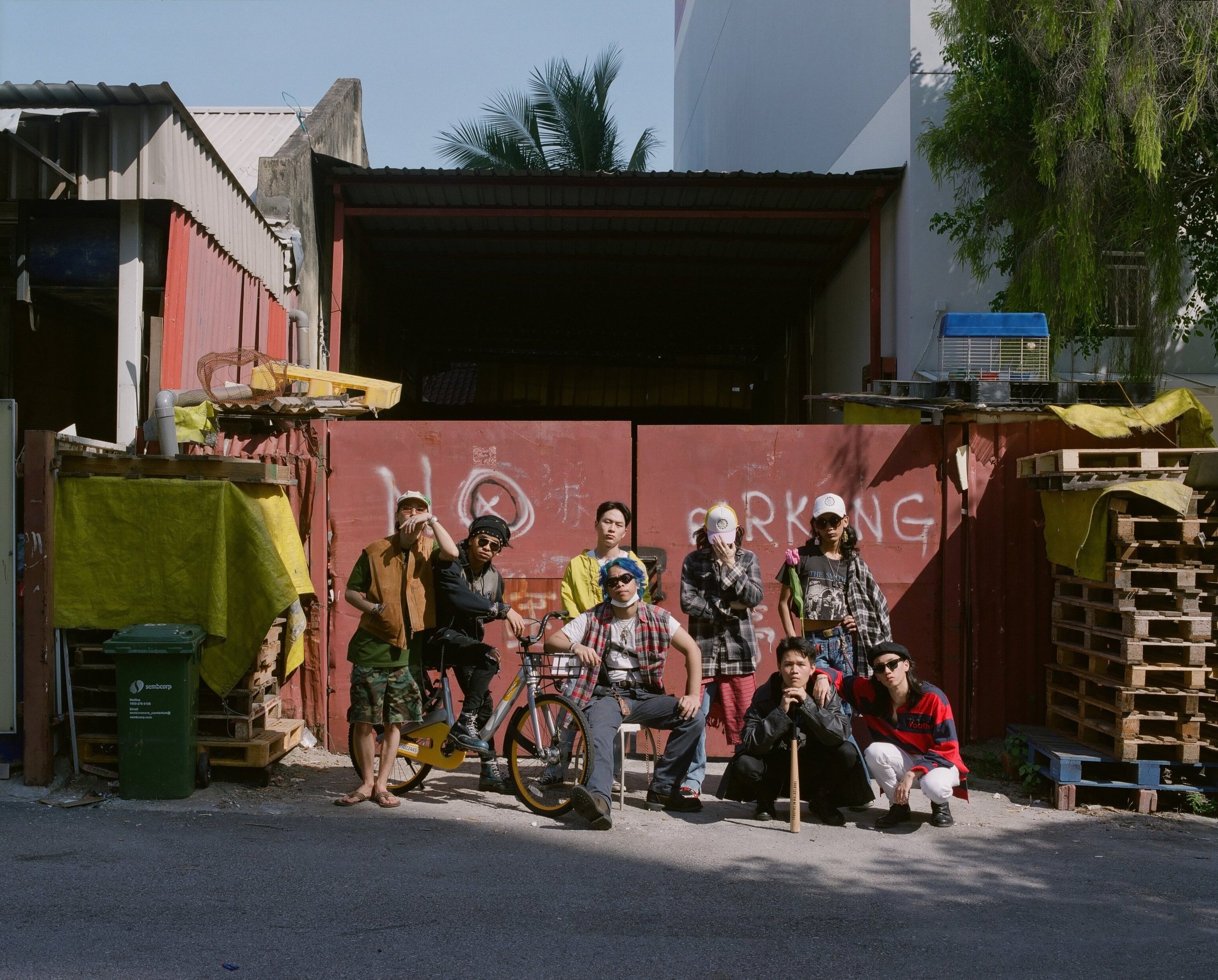 The collective gathered beside a red gate, a bicycle and stacked pallets.