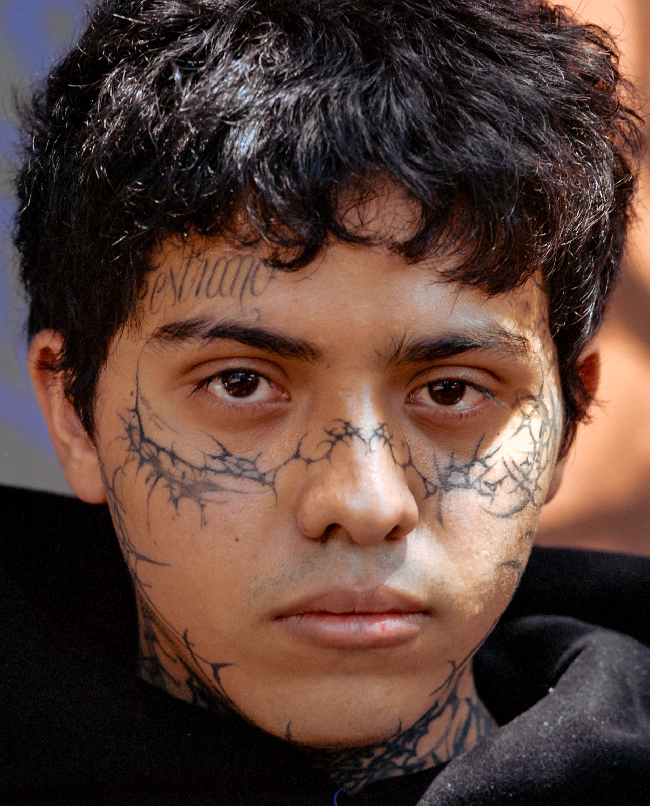 Close frontal portrait of a person with dark curly hair and thorn-like markings across their face, Mexico City, 2024.