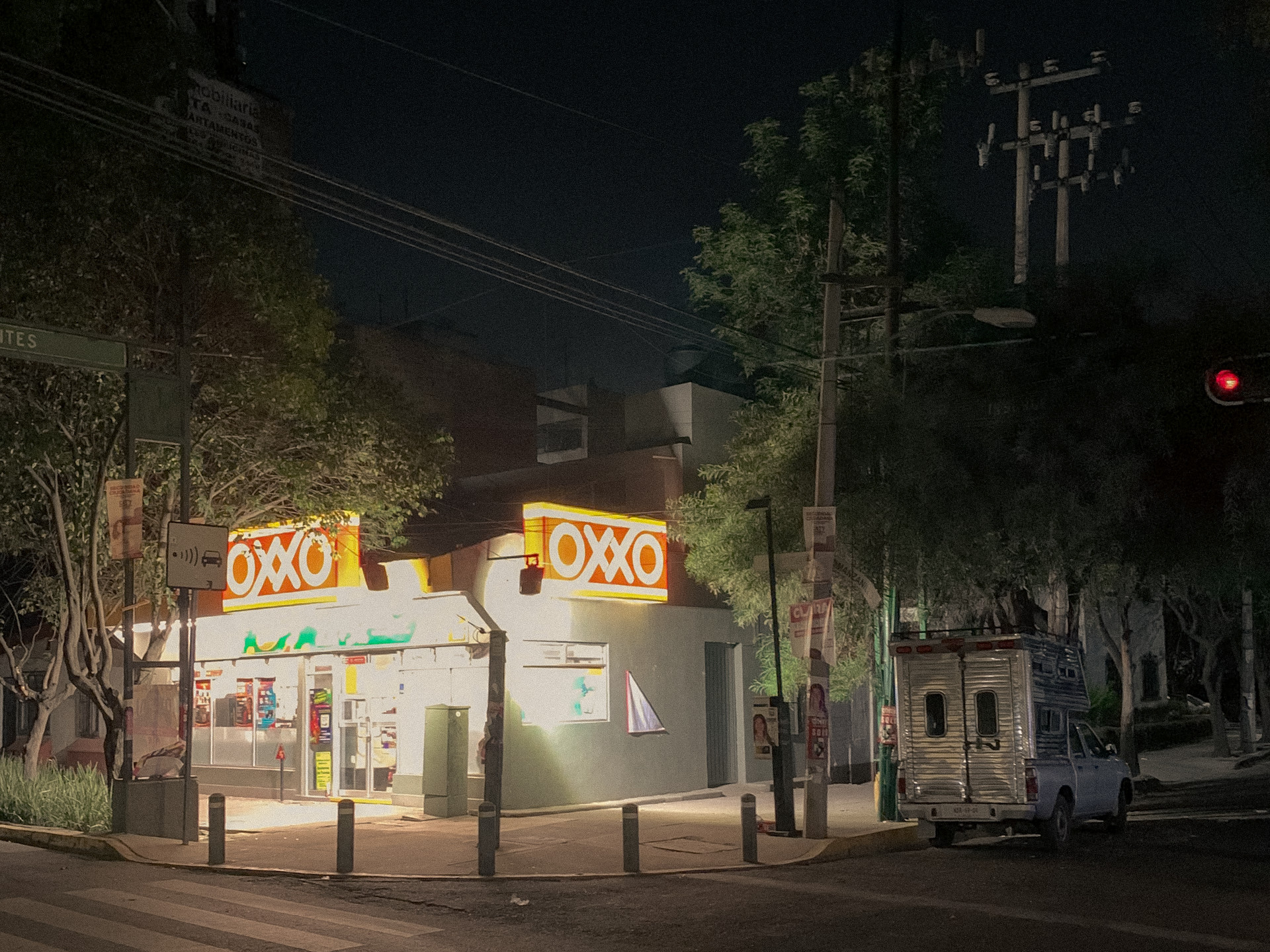 An illuminated convenience store on a dark tree-lined street corner, Mexico City, 2024.
