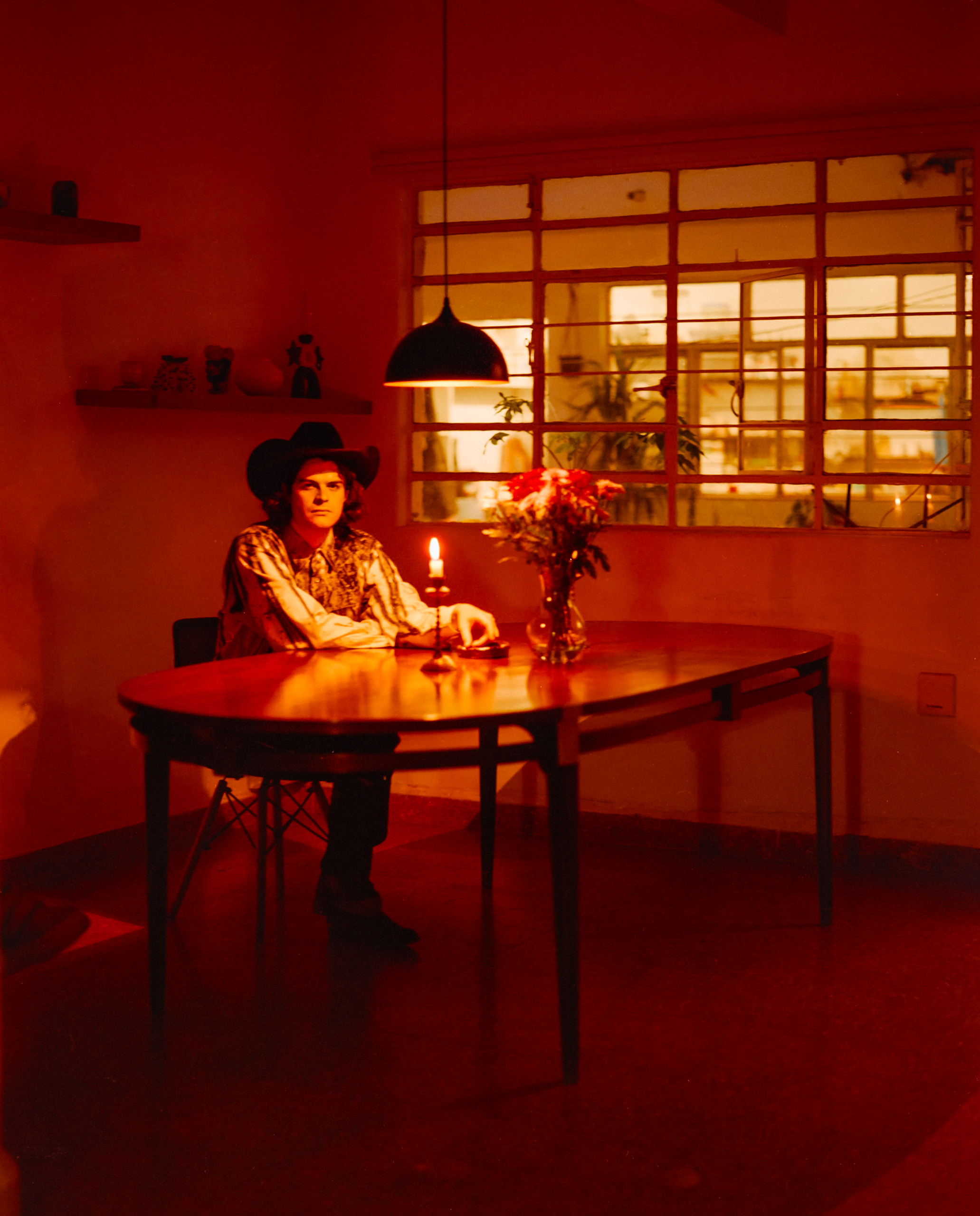 A person seated at a table in a deep red interior with a window and hanging light, Mexico City, 2024.
