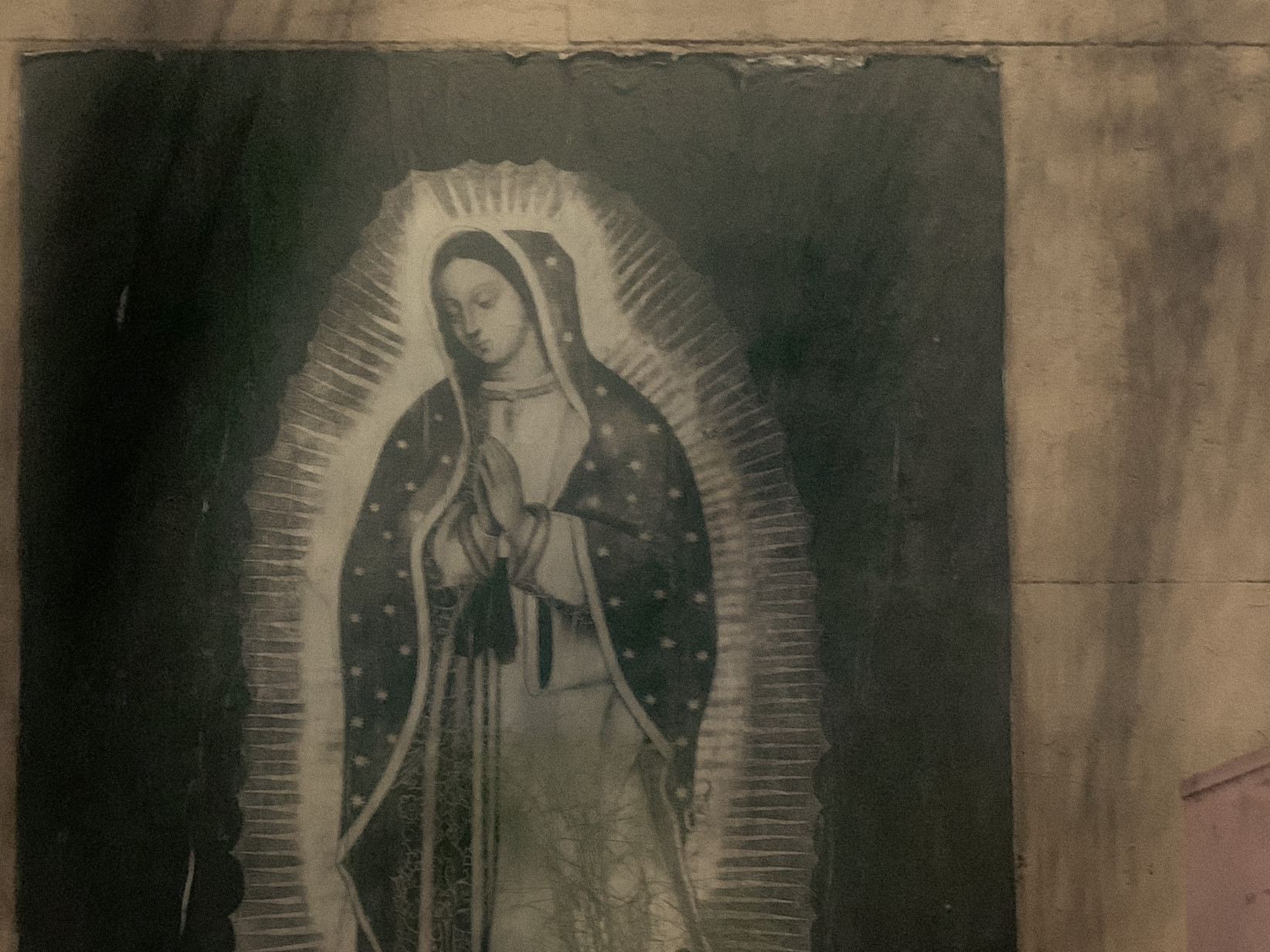 A weathered image of the Virgin of Guadalupe set into a stone wall, Mexico City, 2024.