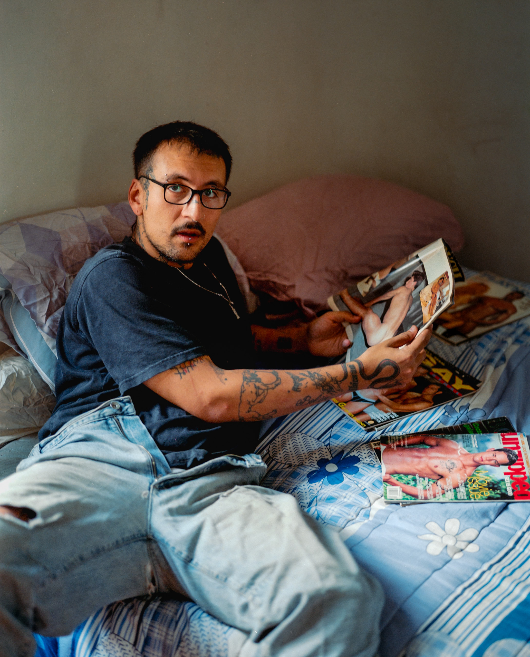 A person with glasses seated on a bed while holding an open publication, Mexico City, 2024.