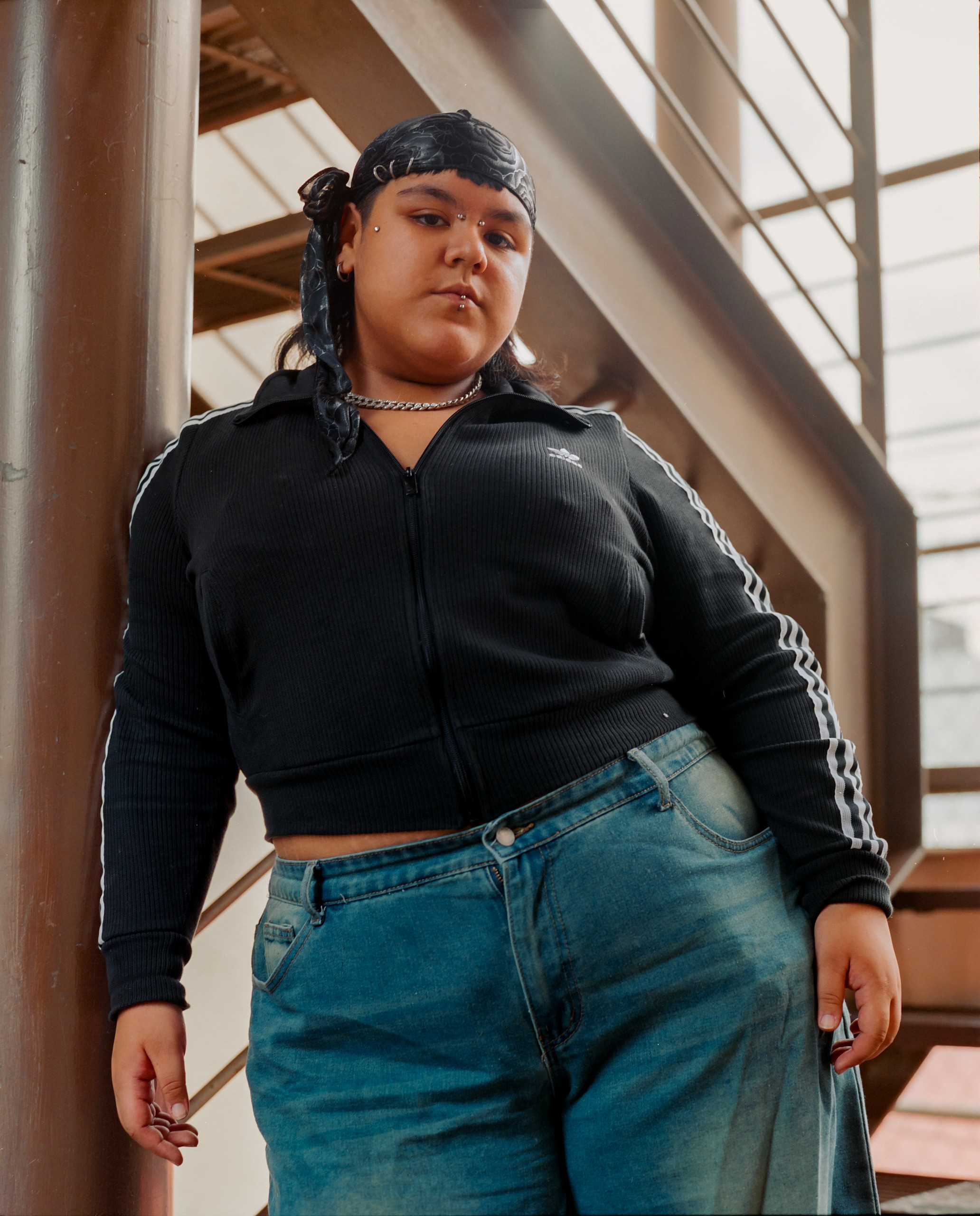 A person in a black top and jeans stands on an interior staircase, Mexico City, 2024.