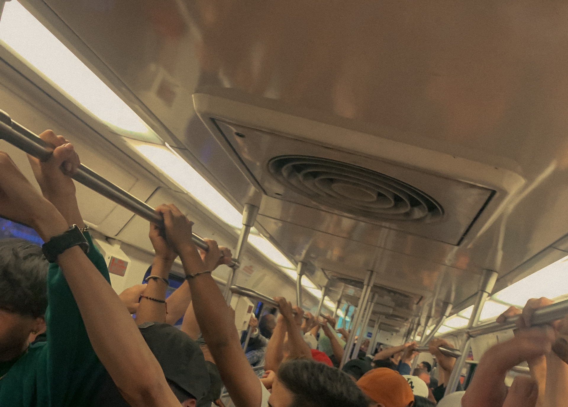 Passengers with raised arms inside crowded public transport beneath fluorescent lights, Mexico City, 2024.