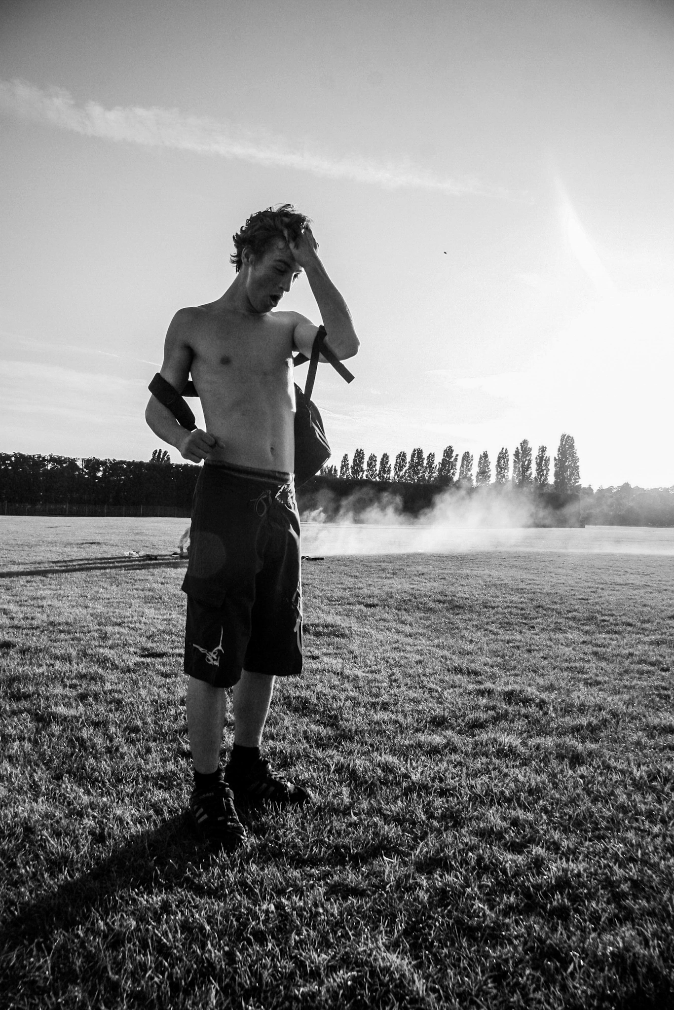 Black-and-white photograph: a person standing in an open field beneath a bright sky.