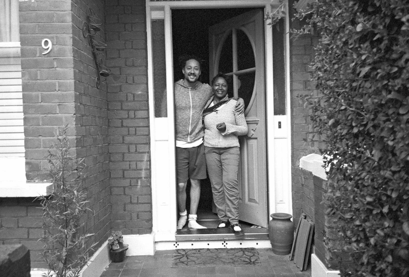 Black-and-white photograph: two people standing in the doorway of a brick house.