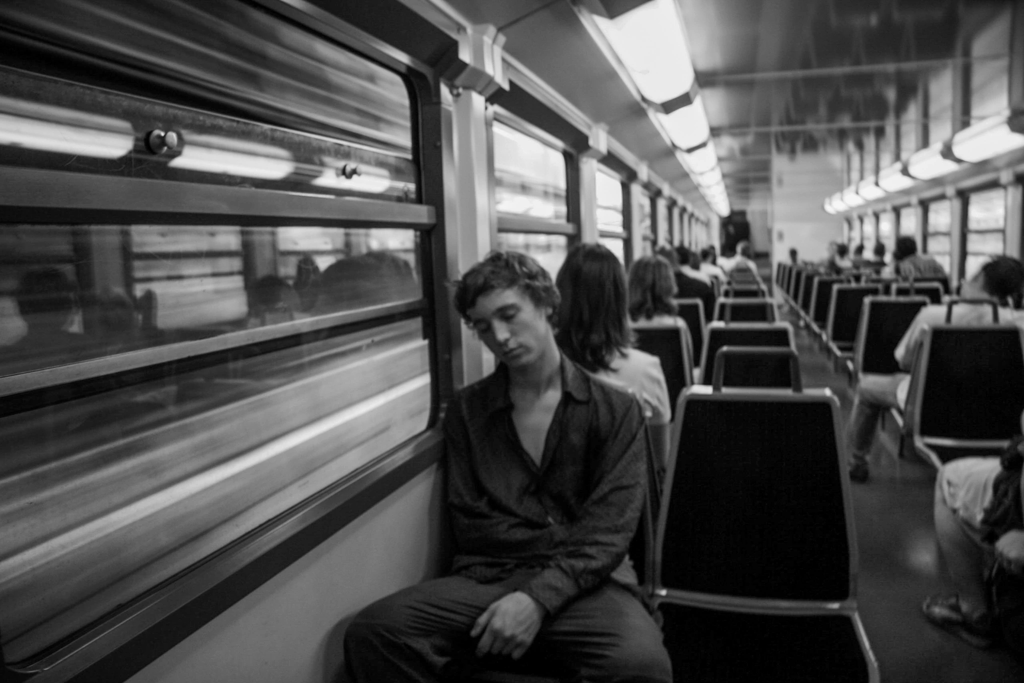 Black-and-white photograph: a person sitting beside a train window.