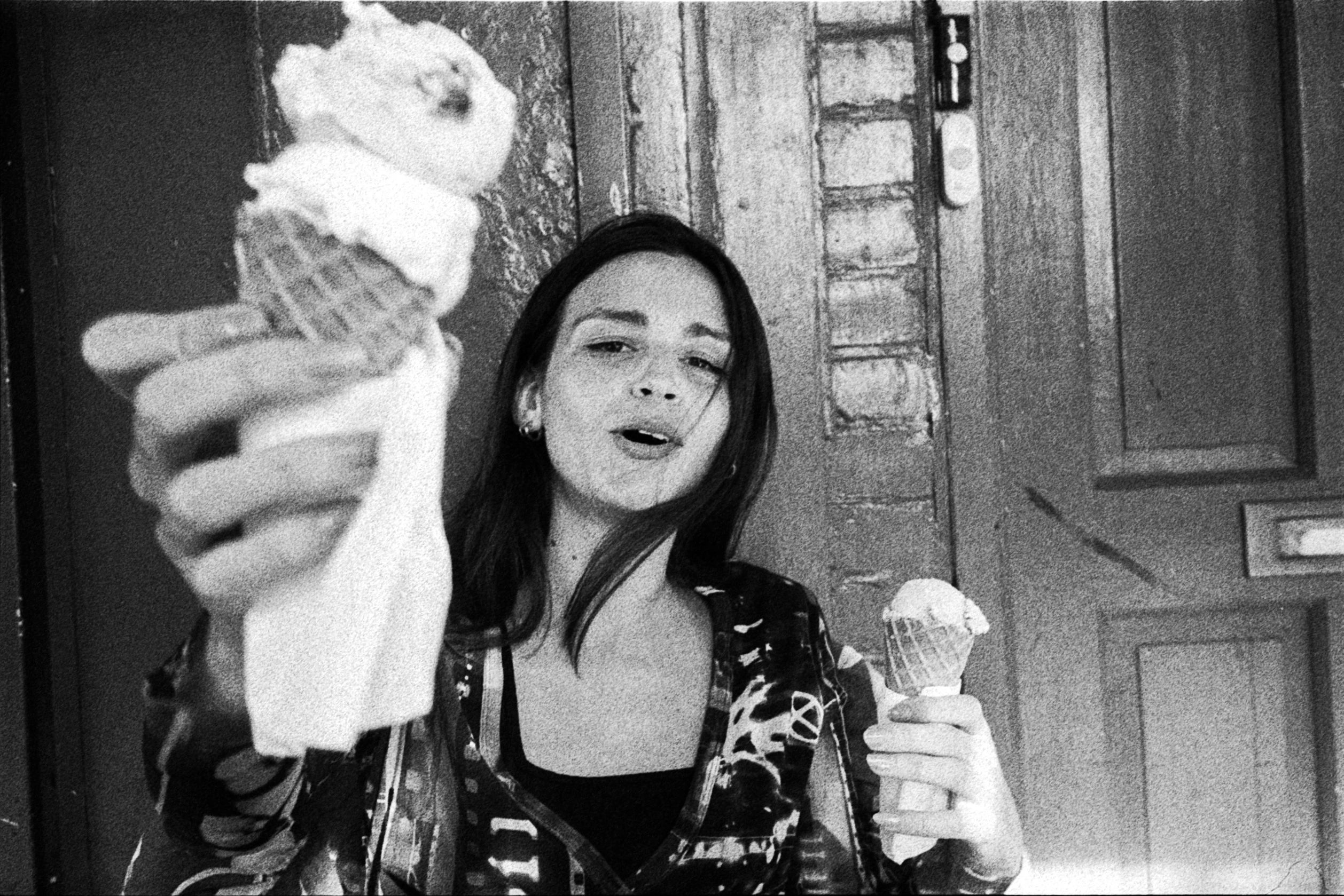 Black-and-white photograph: a person holding an ice cream towards the camera.