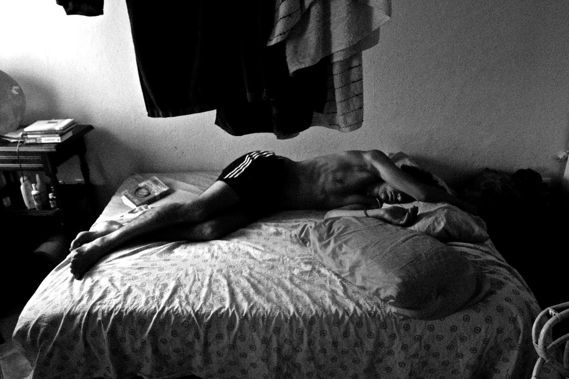Black-and-white photograph: a person lying on a bed beside a window.
