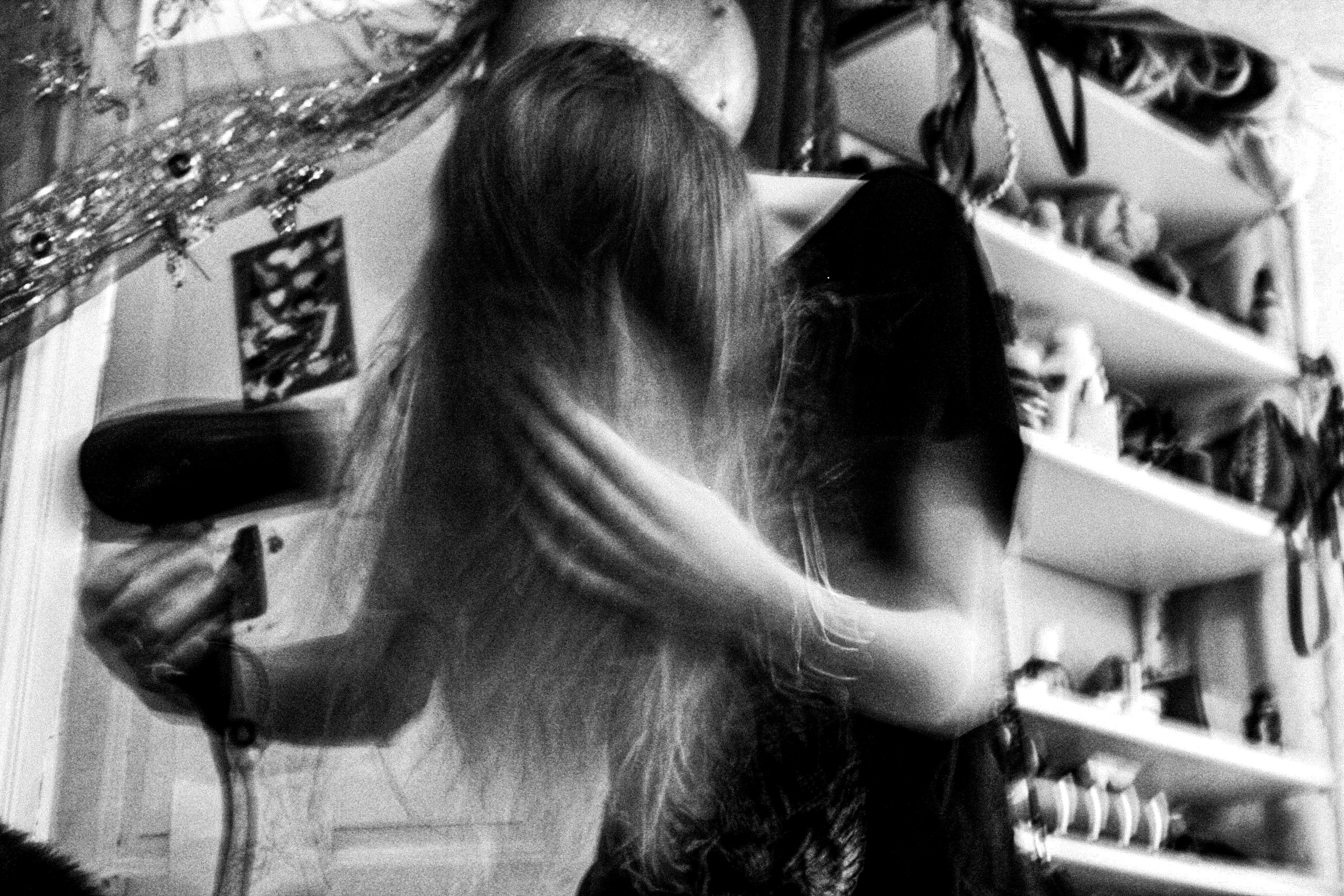 Black-and-white photograph: a person with long hair in a kitchen.