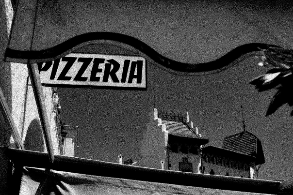 Black-and-white photograph: a pizzeria sign above the street.