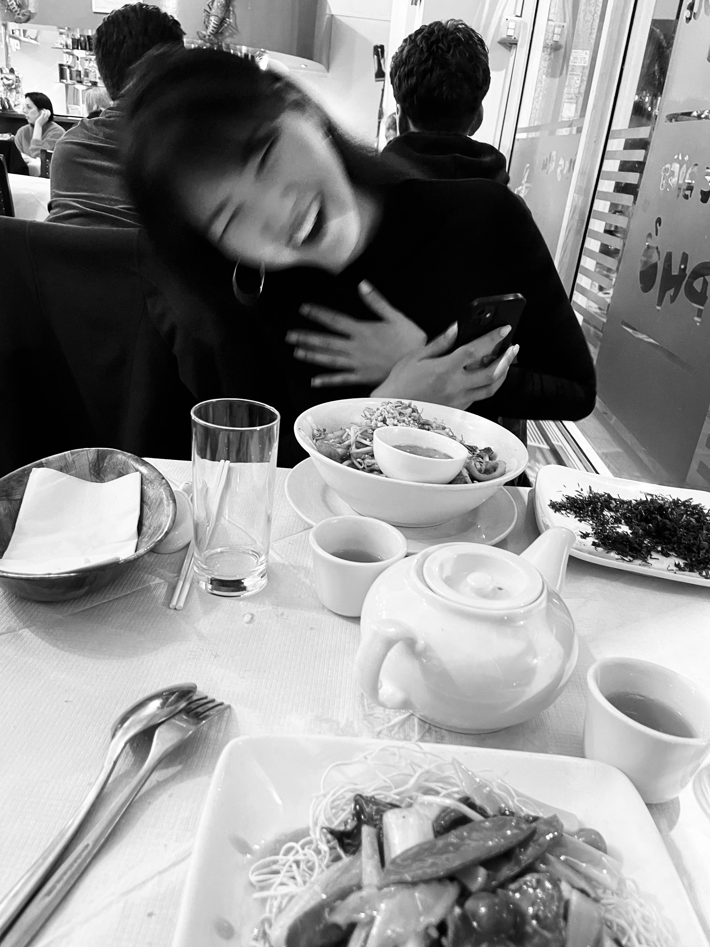Black-and-white photograph: a person at a café table set with cups and plates.