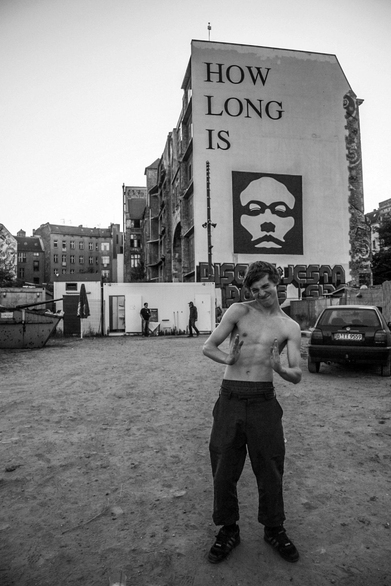 Black-and-white photograph: a person beneath a large painted sign in the city.