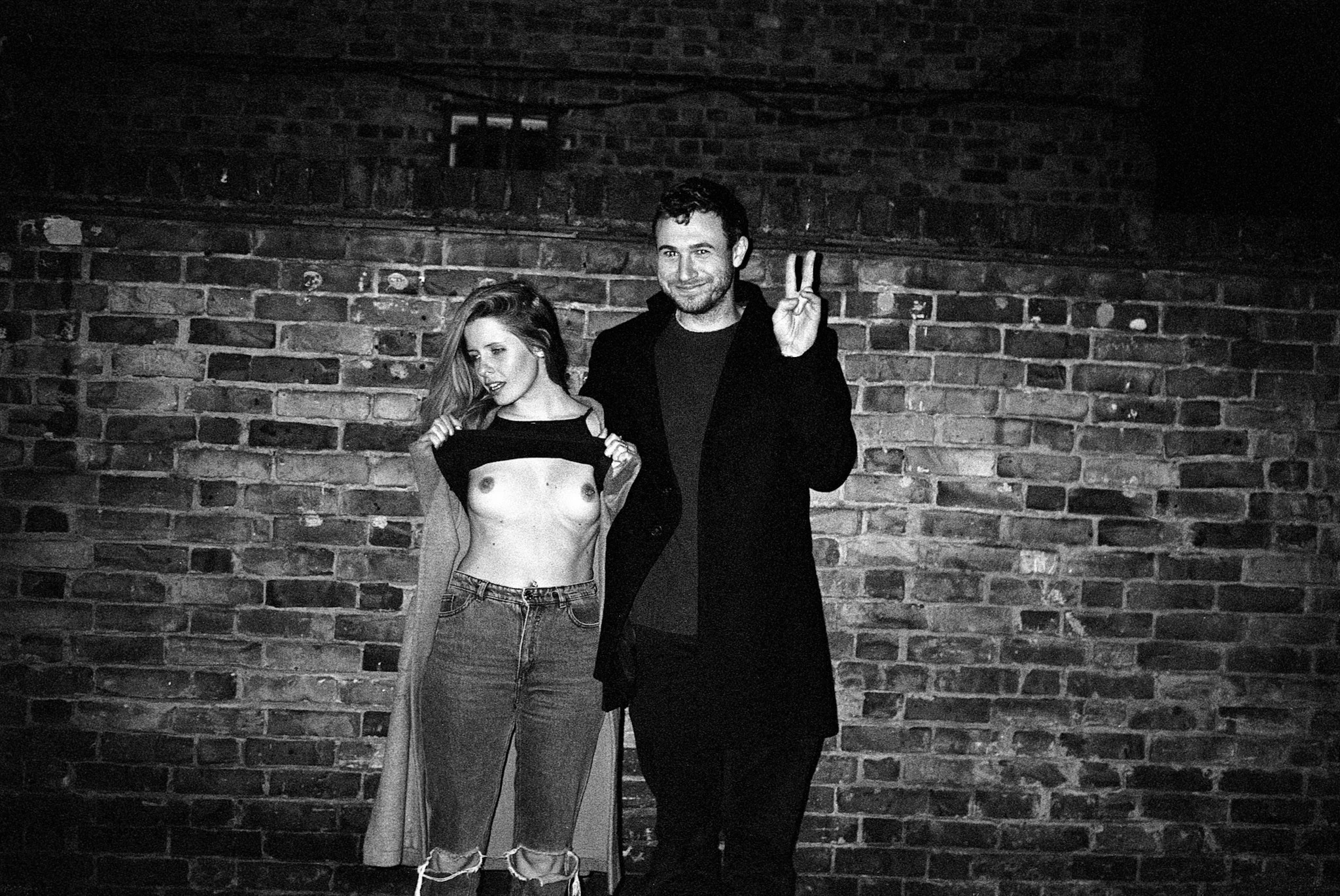 Black-and-white photograph: two people posing together against a brick wall.