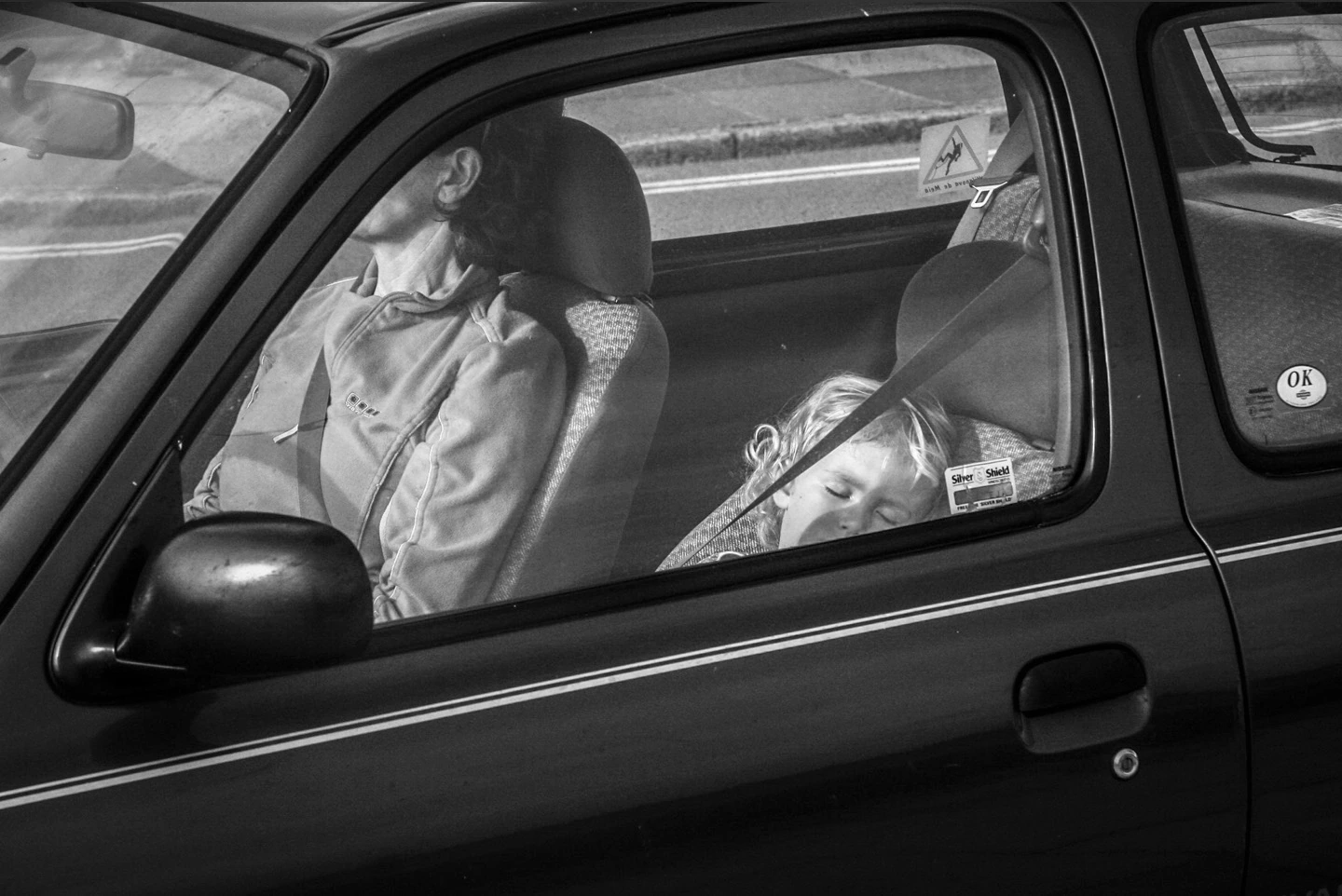 Black-and-white photograph: a person sitting in a car beside an empty passenger seat.
