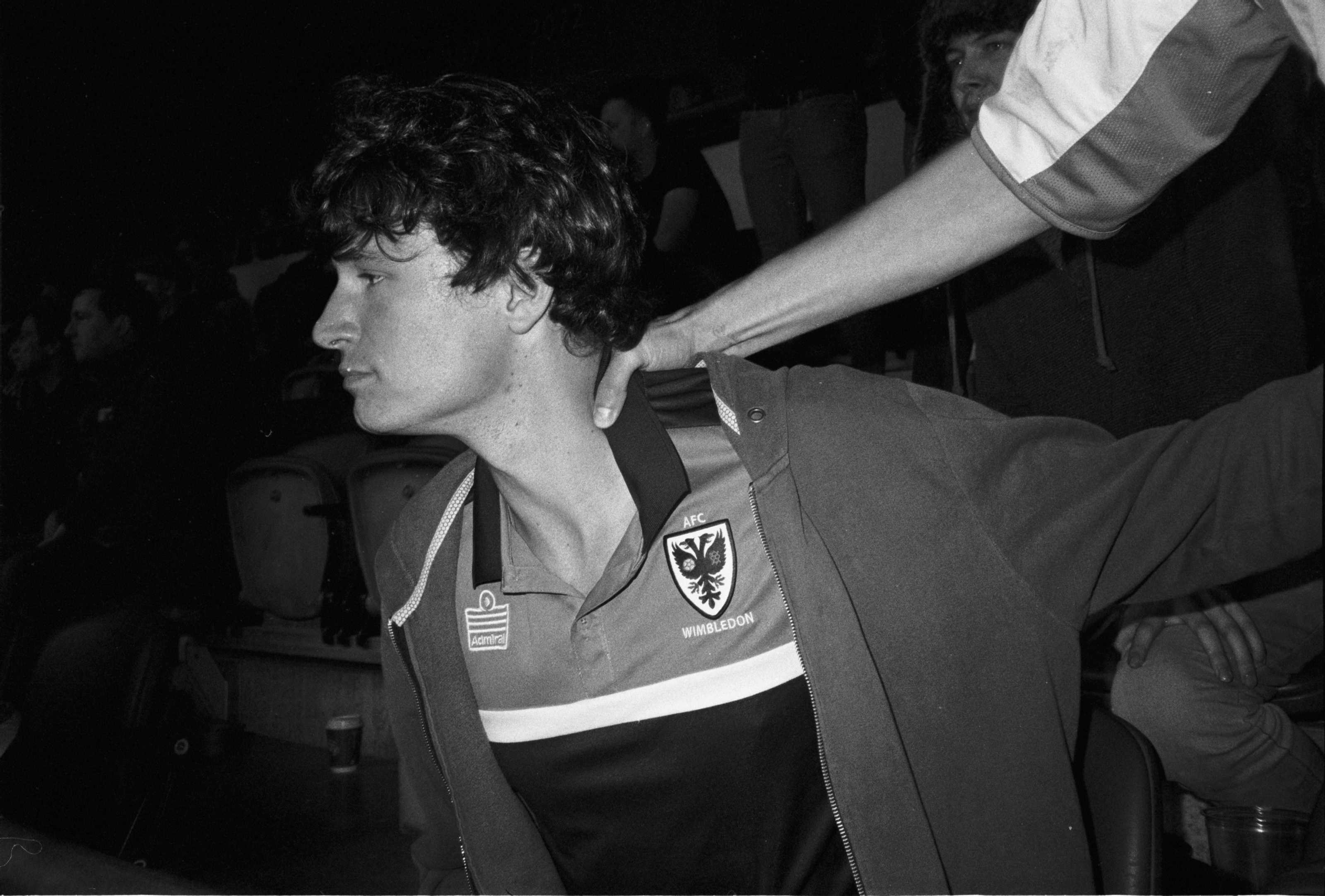 Black-and-white photograph: a person looking to the side as someone rests a hand on their shoulder.