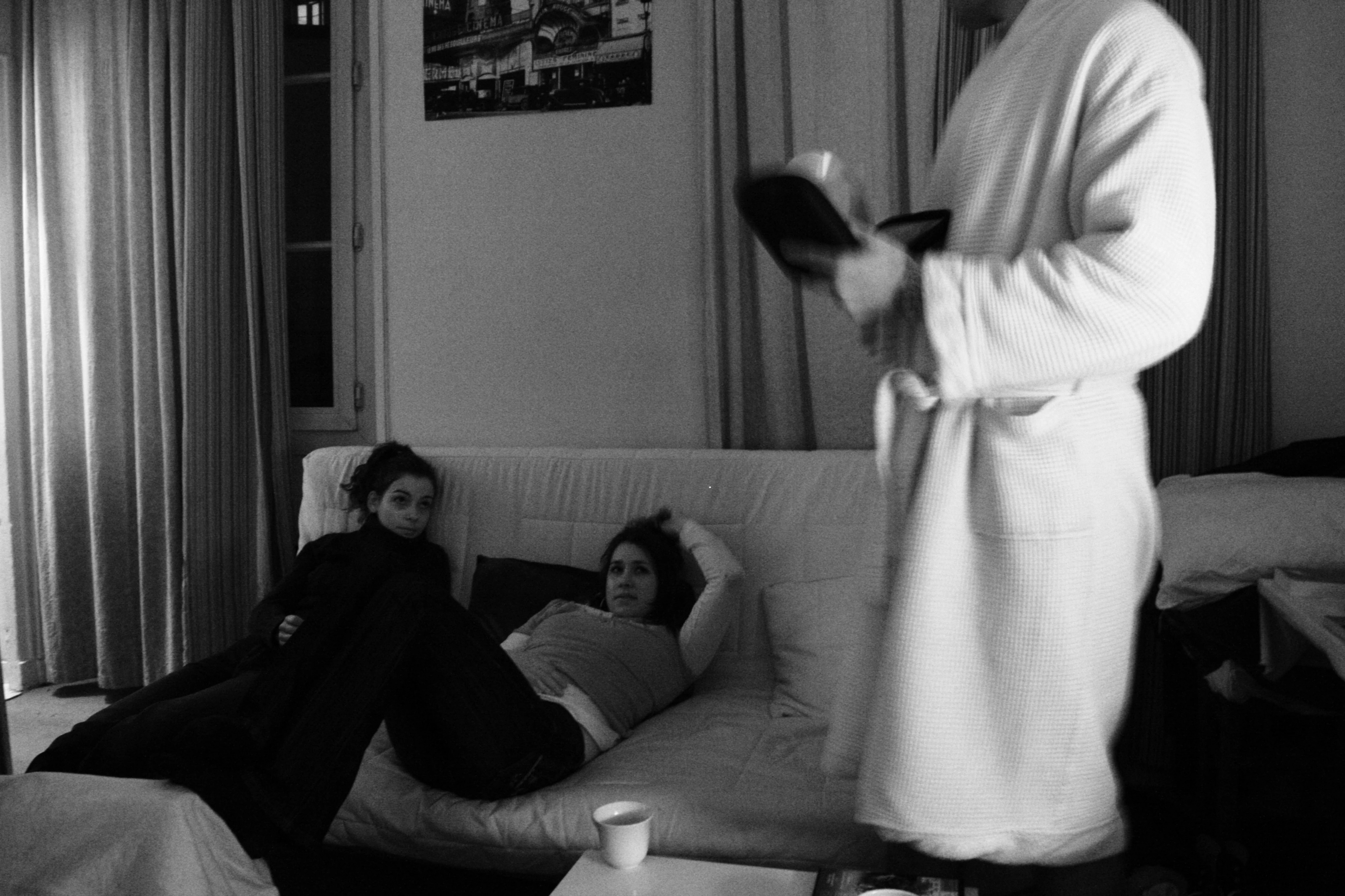 Black-and-white photograph: three people in a room, one standing in the foreground.