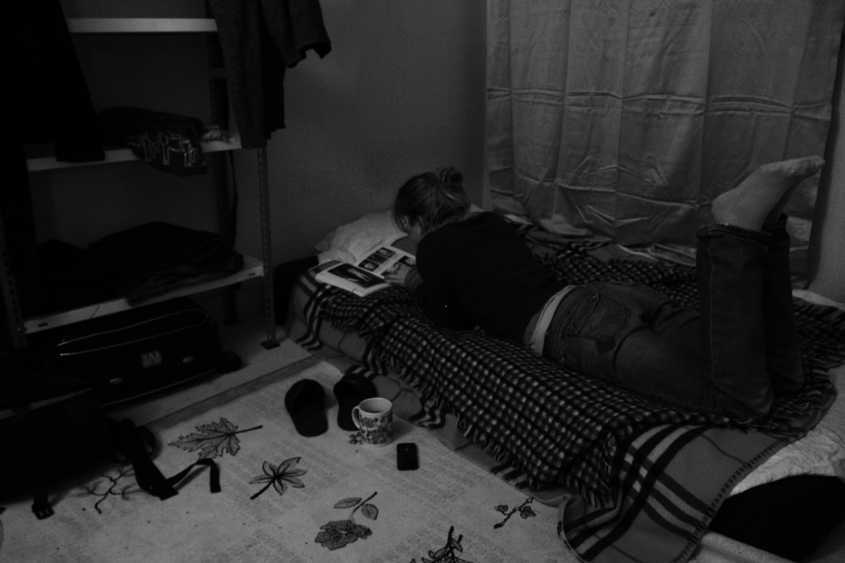 Black-and-white photograph: a person lying on the floor of a dimly lit room.