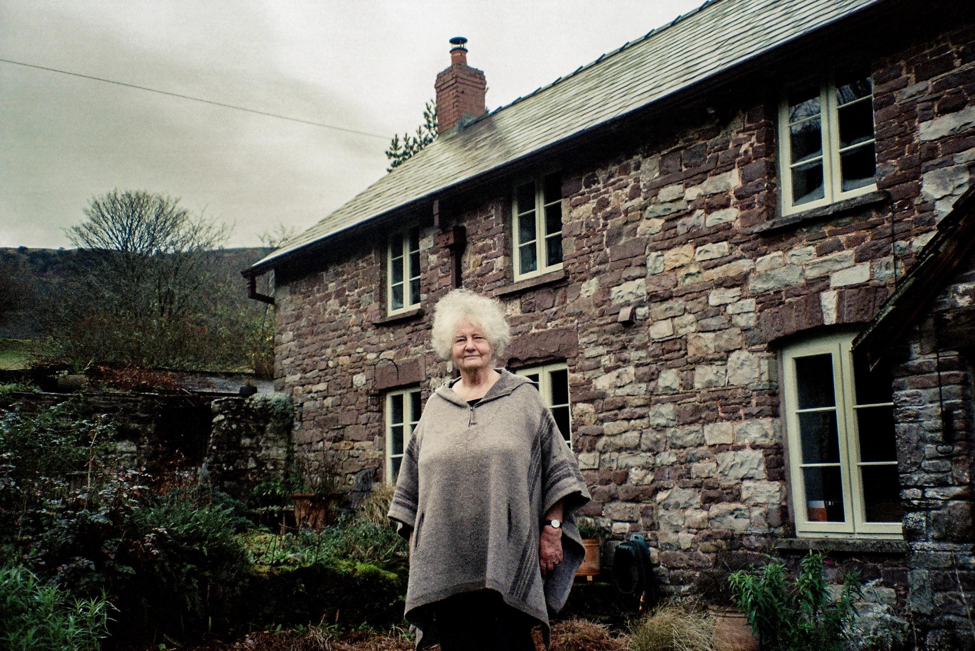 Woman outside stone cottage.