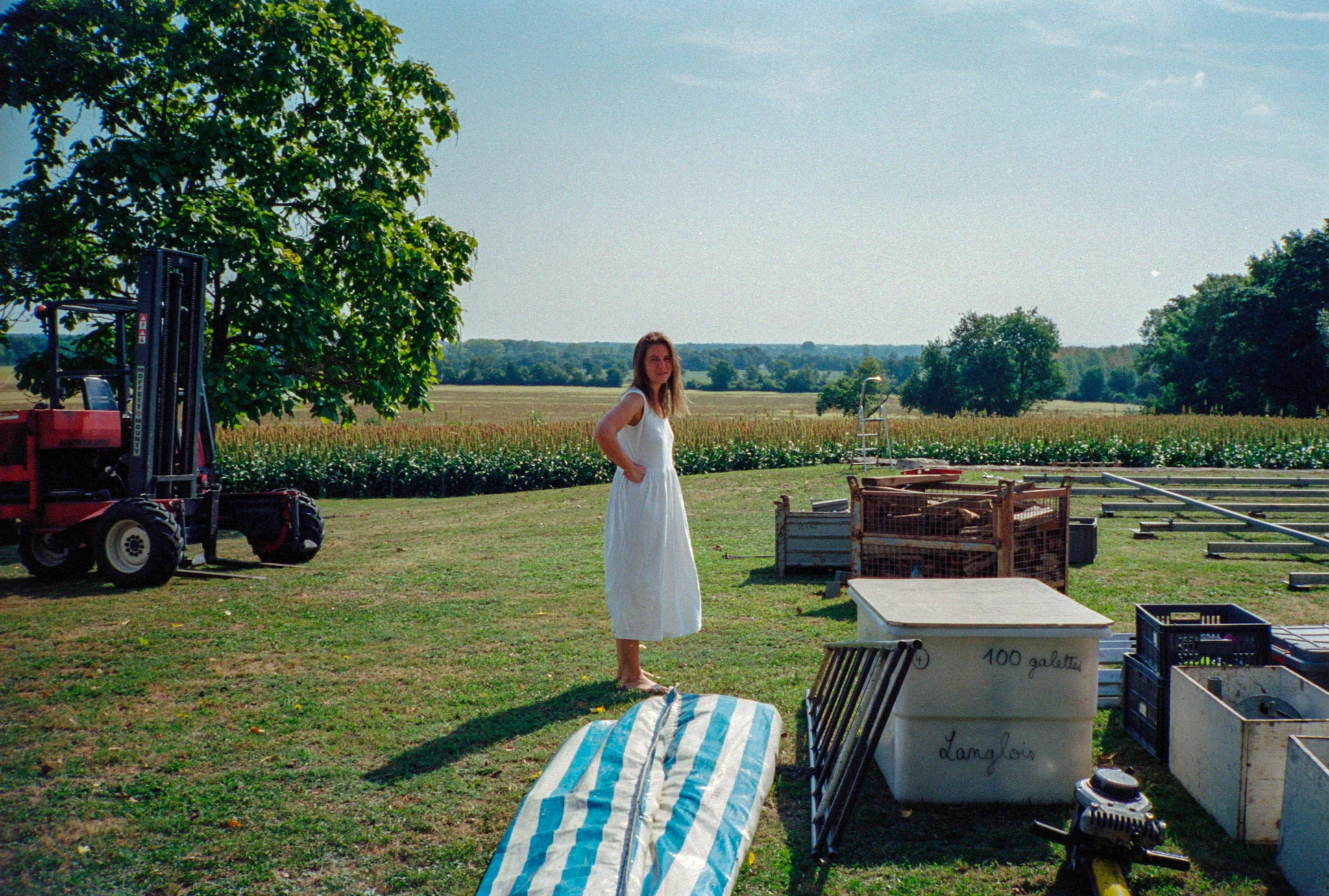 Woman in white beside boxes outdoors.