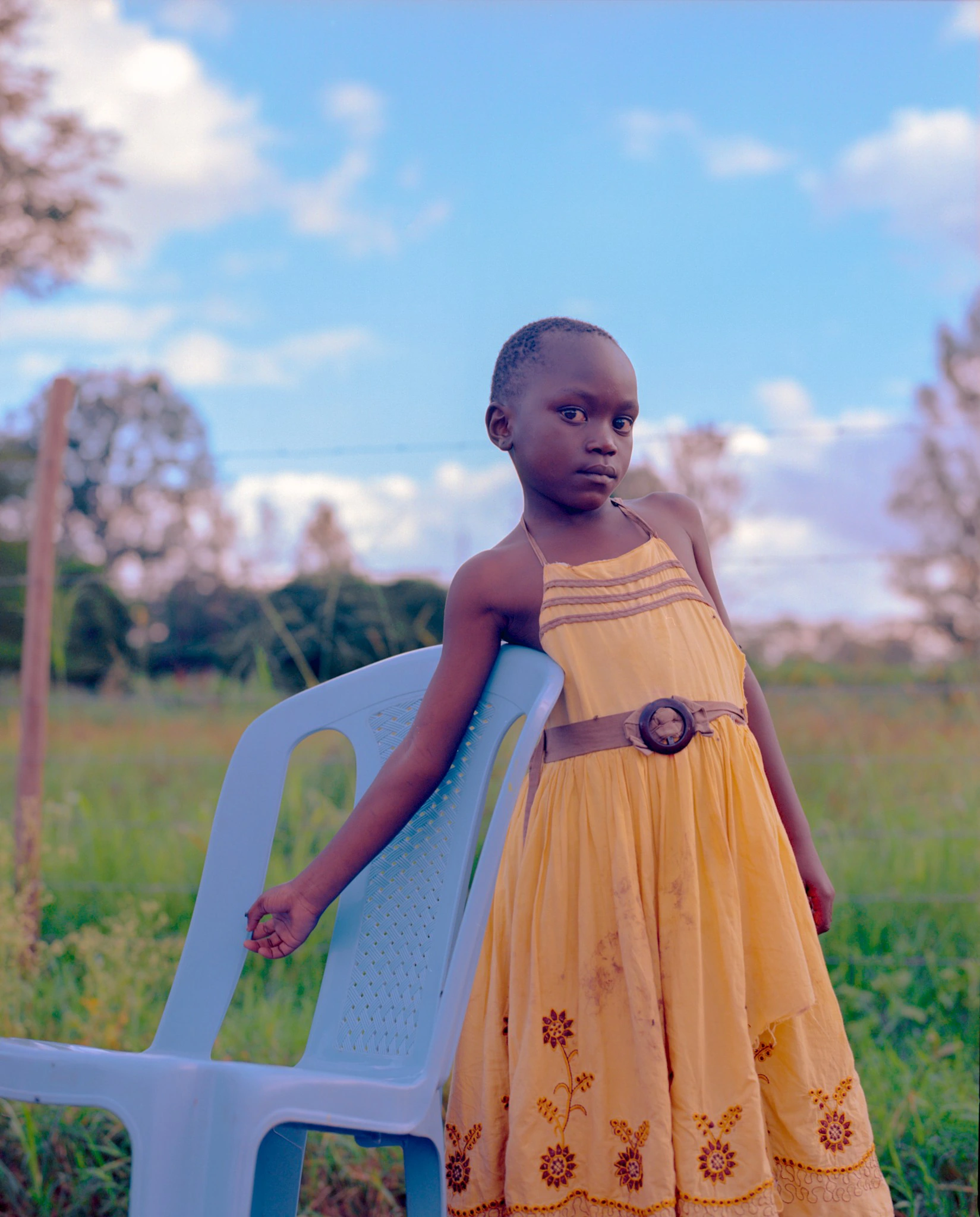 Child in yellow dress beside chair.
