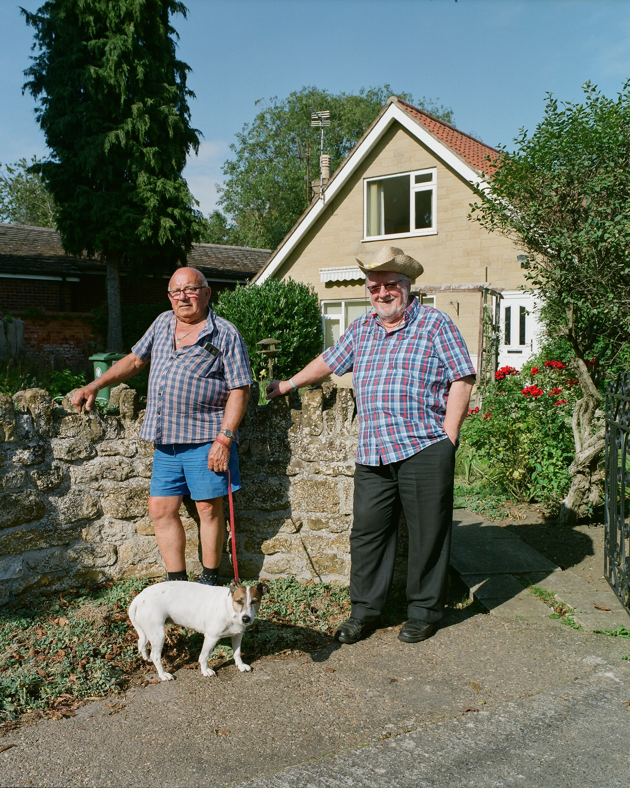 Two men and dog beside cottage.