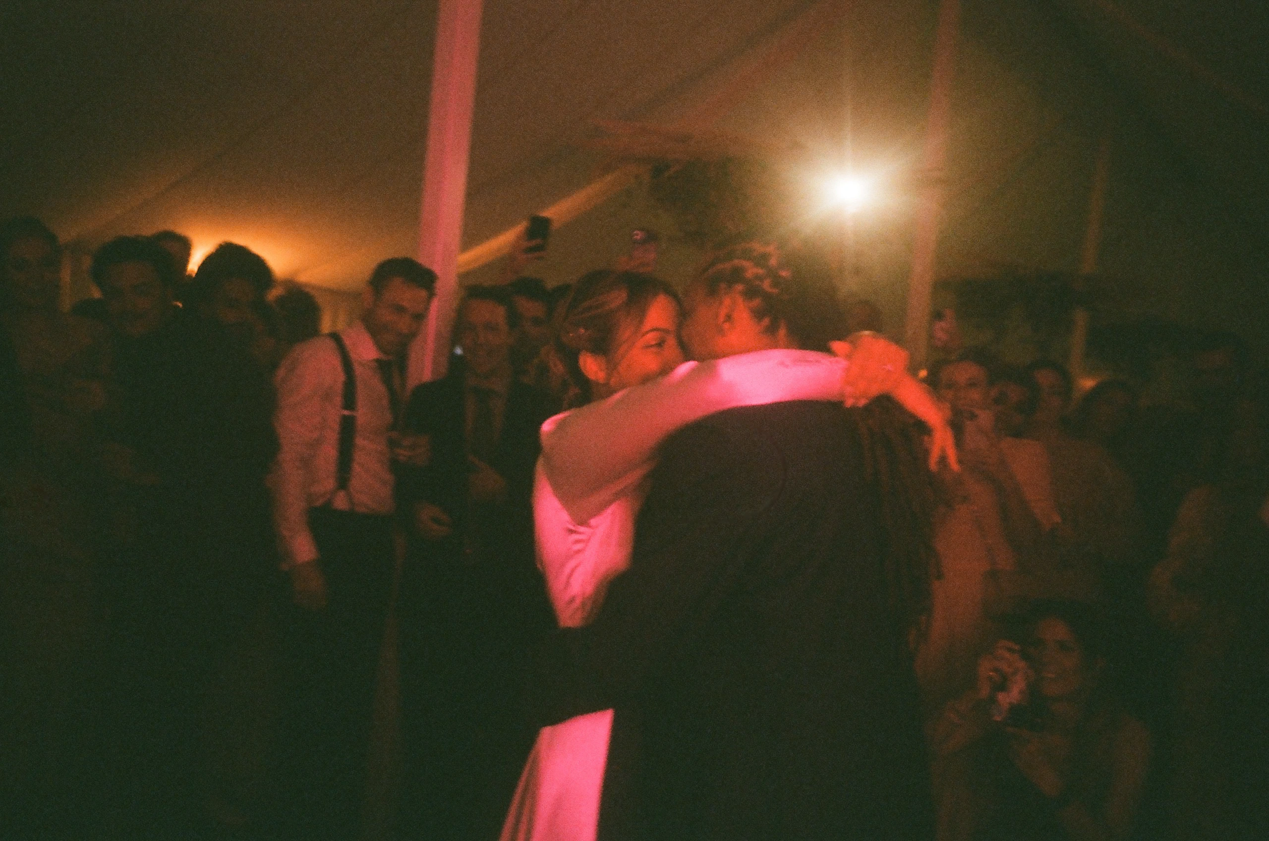 Embrace in red-lit crowd.