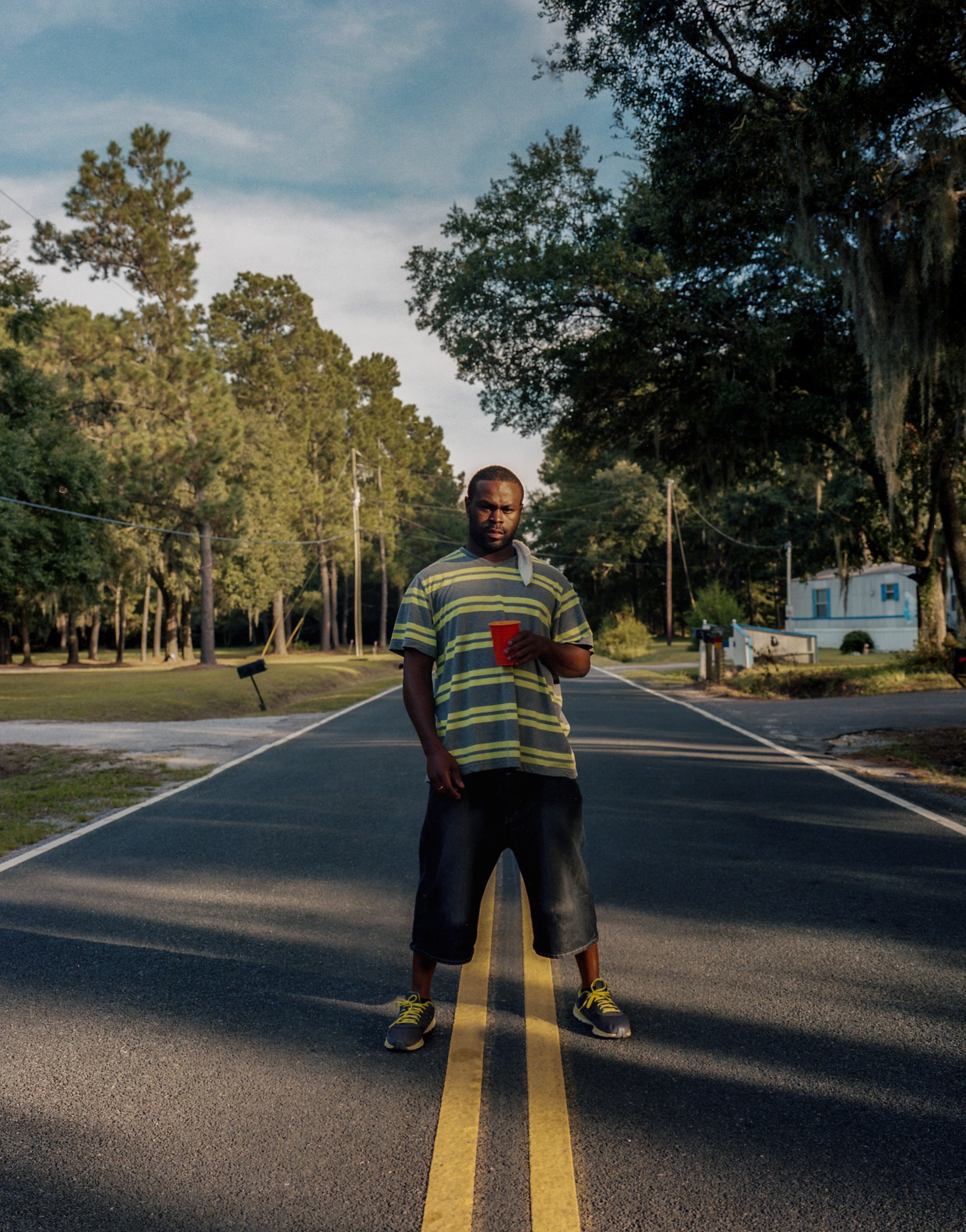 A person standing on the yellow centre lines of a road, with houses and trees behind.