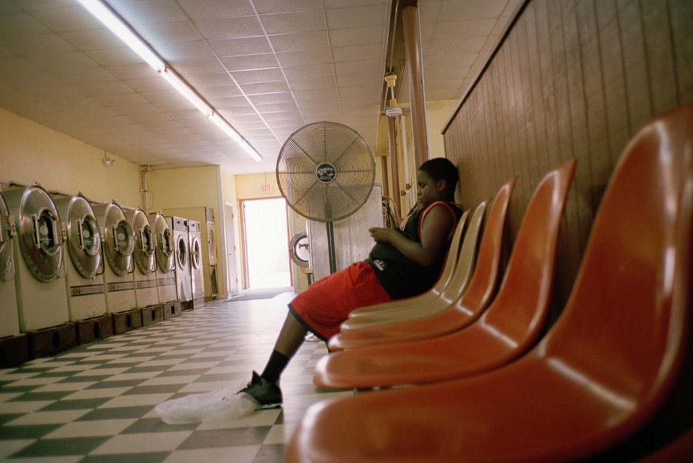 A person seated among orange chairs in a laundrette.
