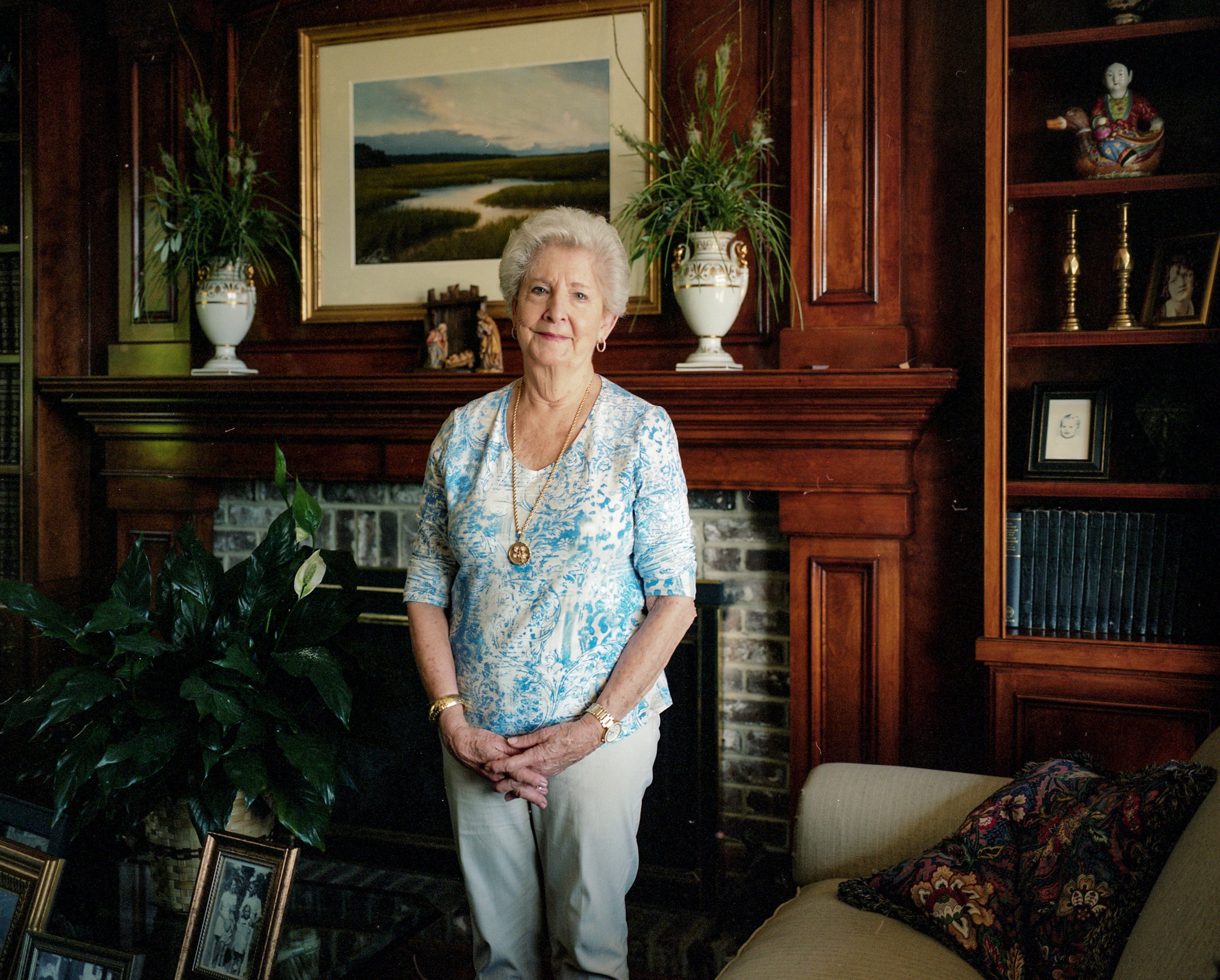 A woman standing in a wood-panelled room beneath a landscape painting.