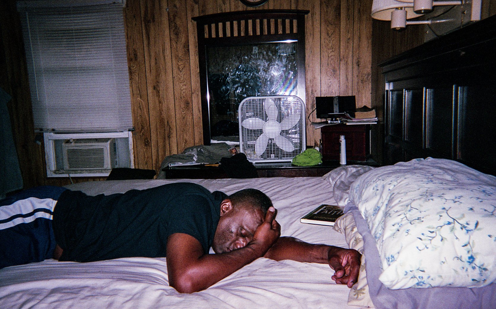 A person lying on a bed in a wood-panelled room.