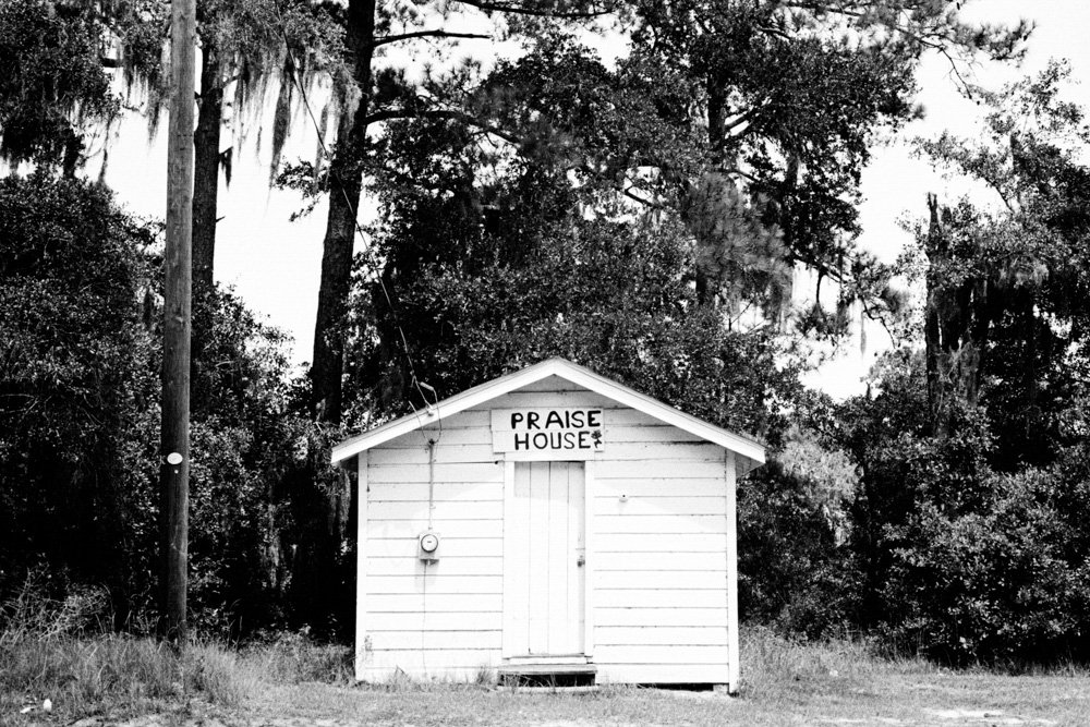 A small white wooden praise house beneath trees.