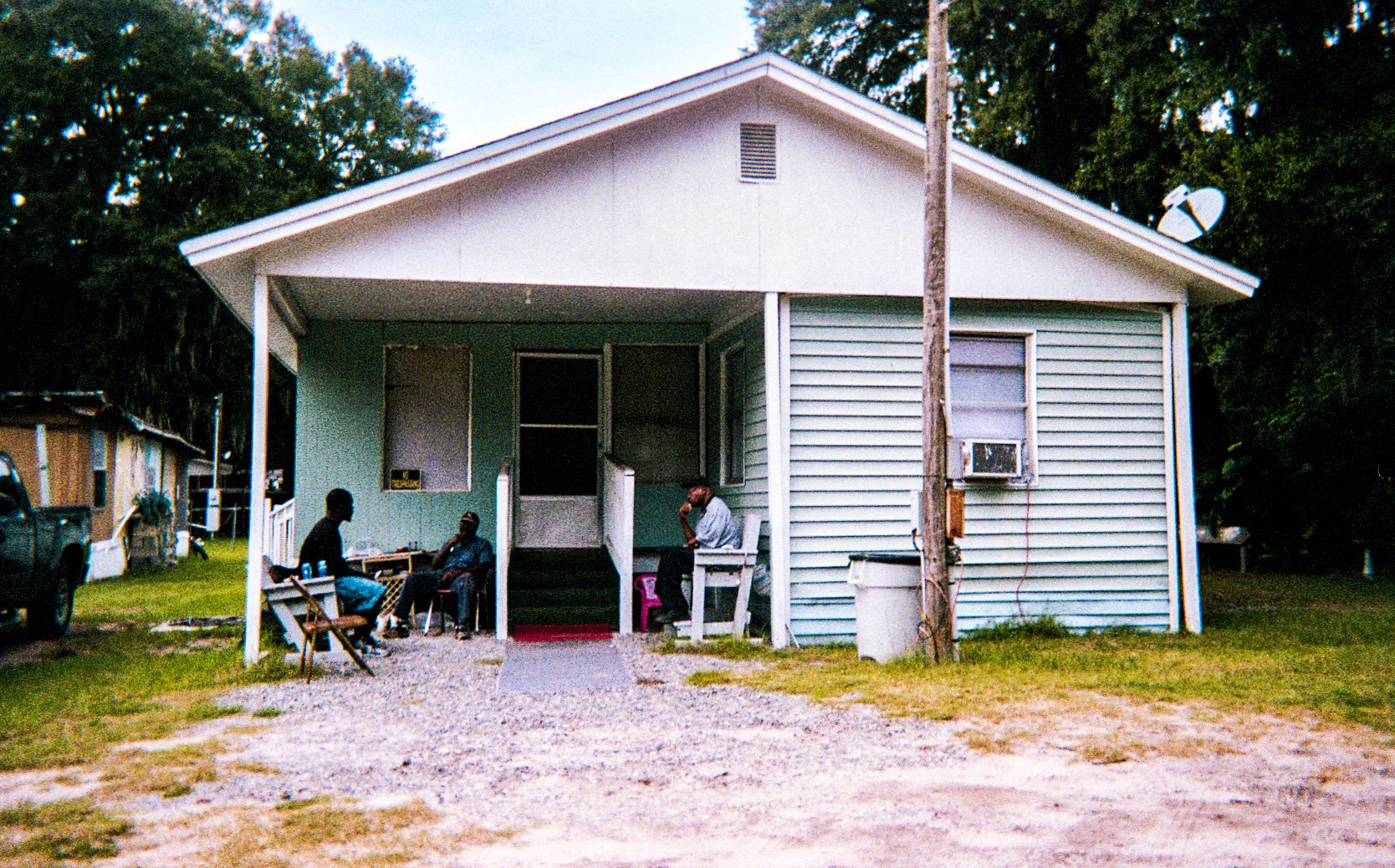 A small wooden house with people and chairs on the porch.