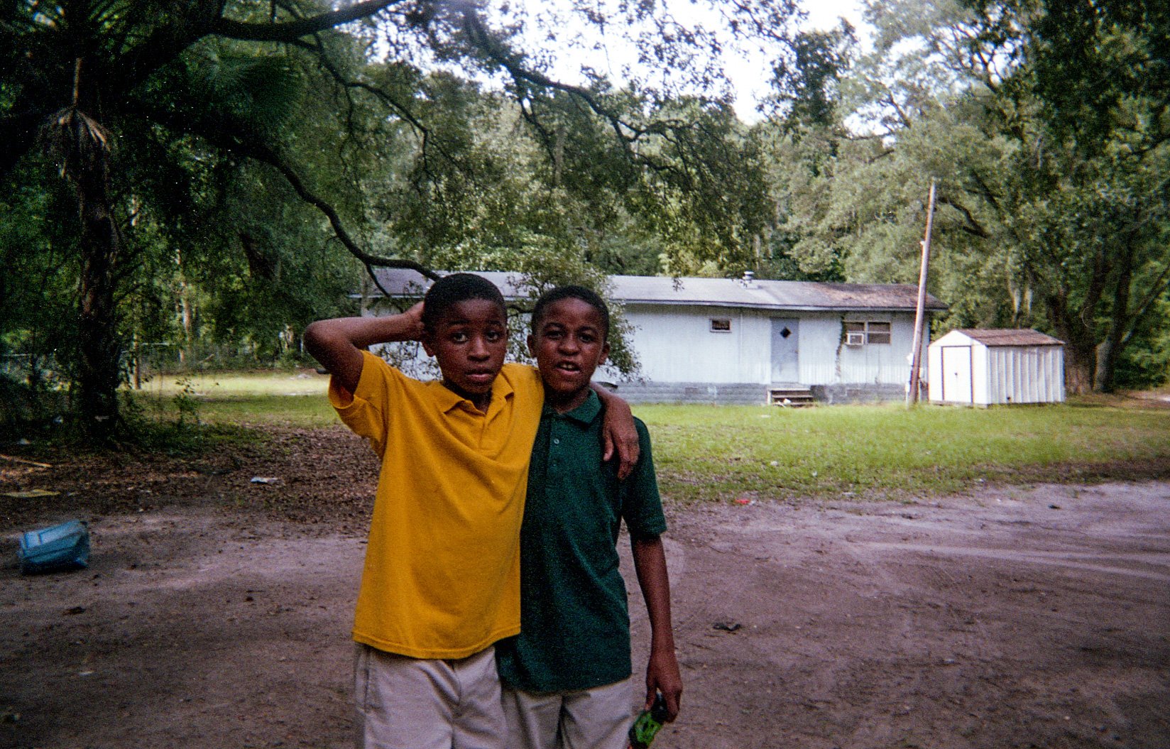 Two children standing together in a yard, with one arm around the other's shoulder.